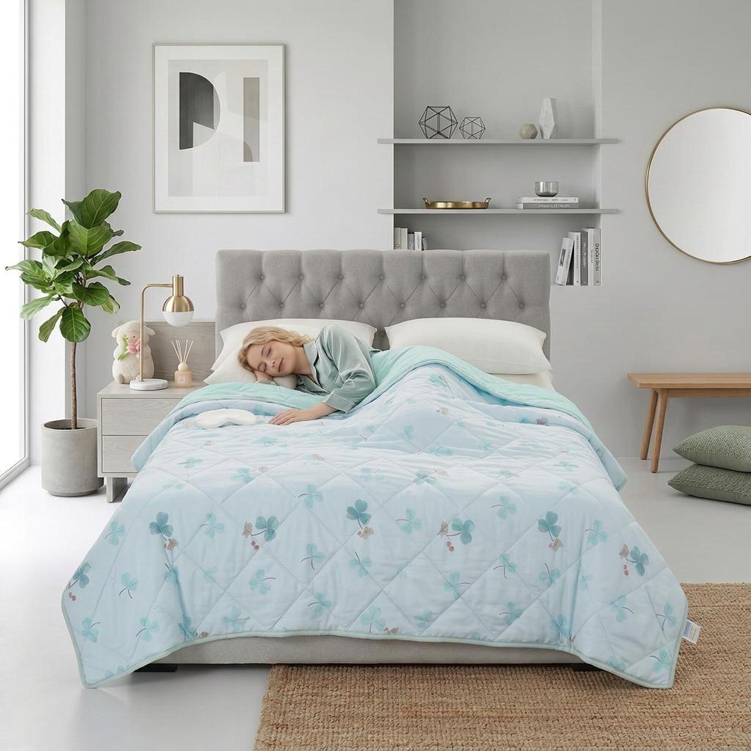 Light blue quilted cooling blanket with green clover pattern on a bed with a sleeping person.