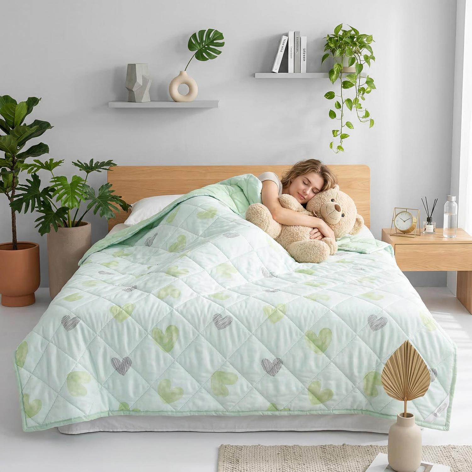 Woman sleeping peacefully under a light green quilted cooling blanket with heart patterns, hugging a teddy bear.