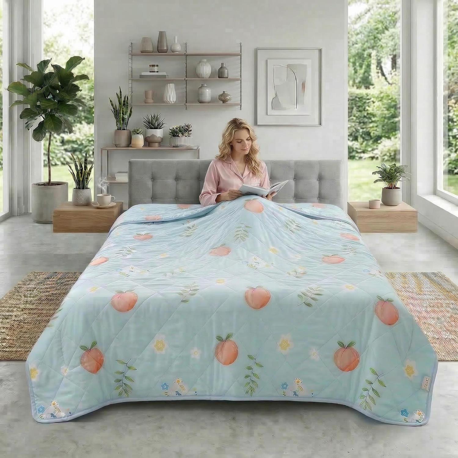 Light blue quilted cooling blanket with peach and floral print on a bed with a woman reading.