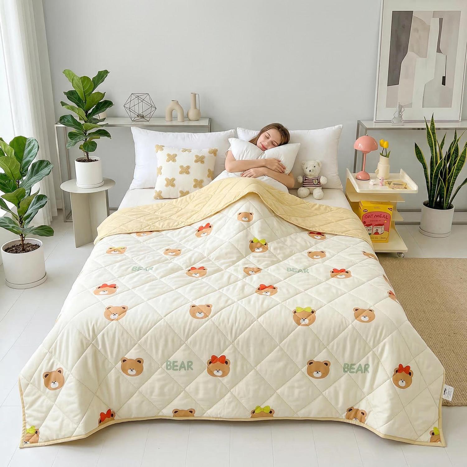 Cream quilted cooling blanket with cute bear print, yellow trim, covering a person in bed.