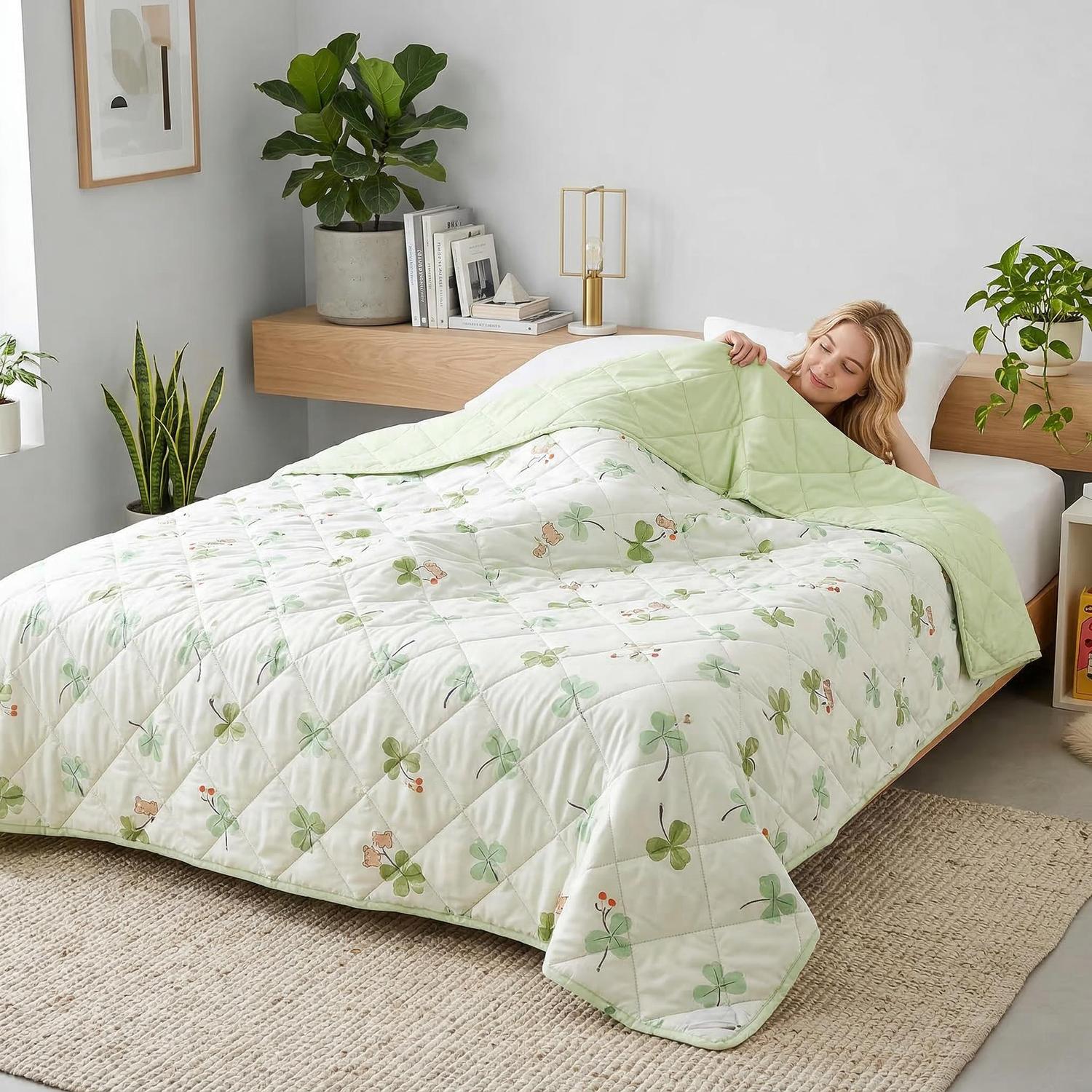 Woman in bed with a white quilted cooling blanket featuring green clover and bear patterns, light green reverse.