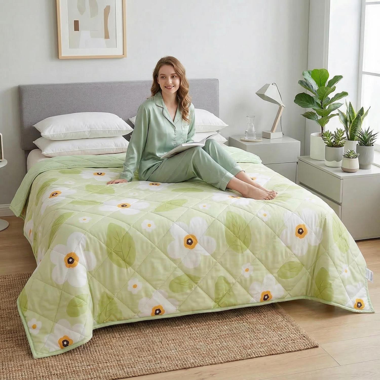 Woman in green pajamas on a bed with a light green quilted cooling blanket featuring white floral print.
