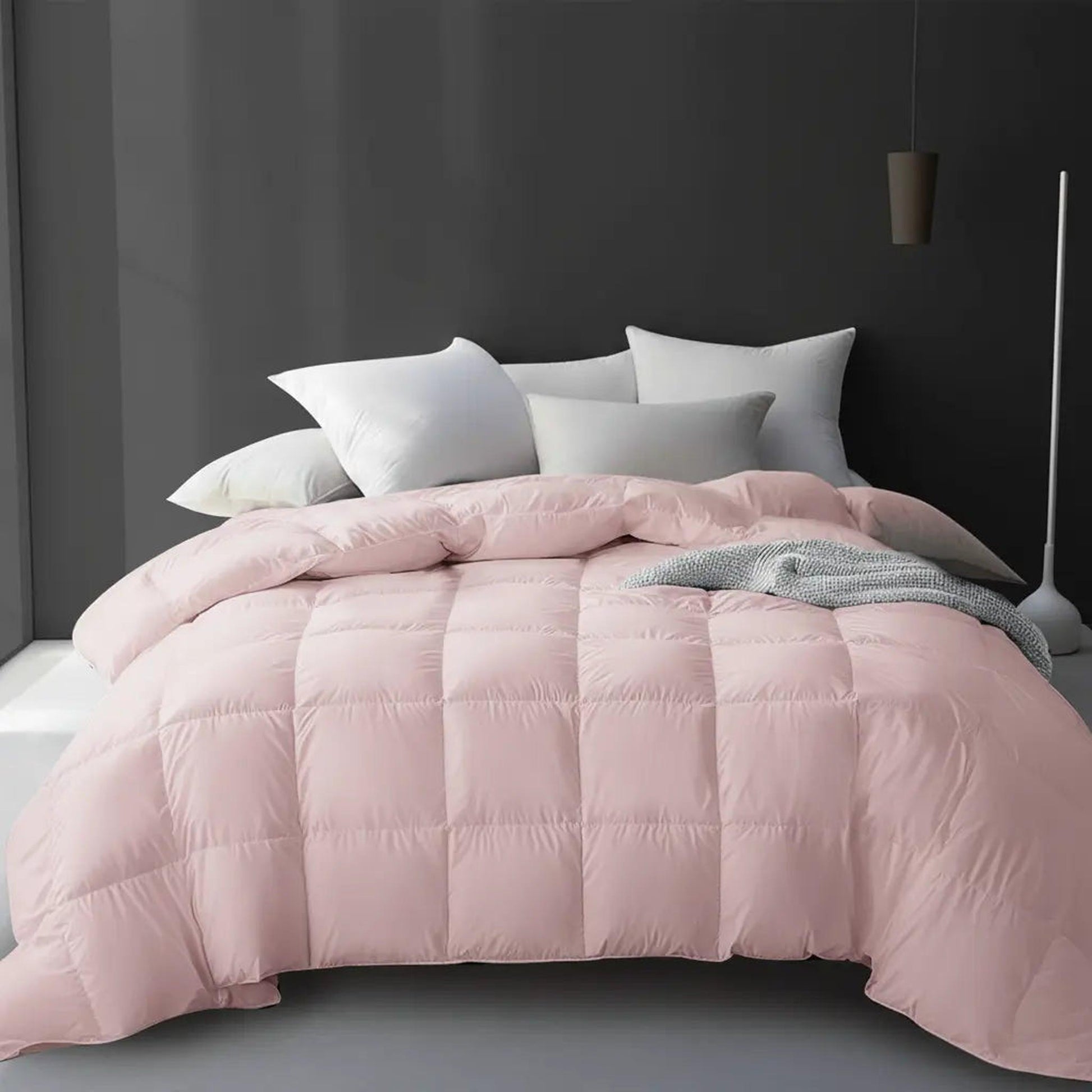 Soft pink goose down comforter with square quilting on a bed with white pillows.