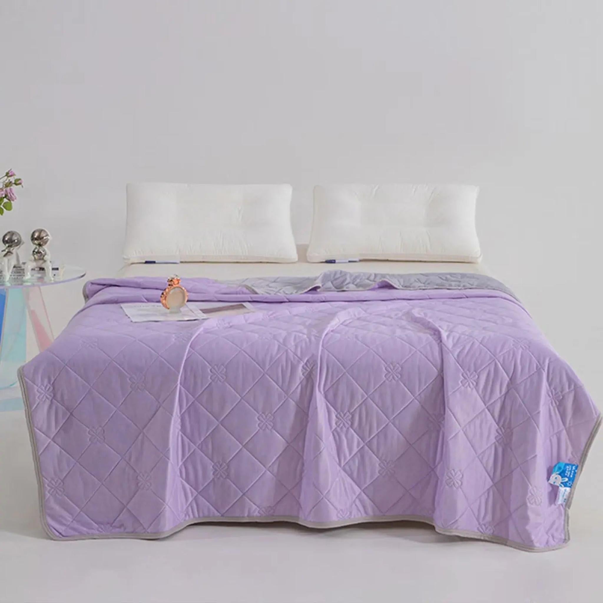 Light purple quilted cooling blanket with gray reverse, draped over a bed with white pillows.