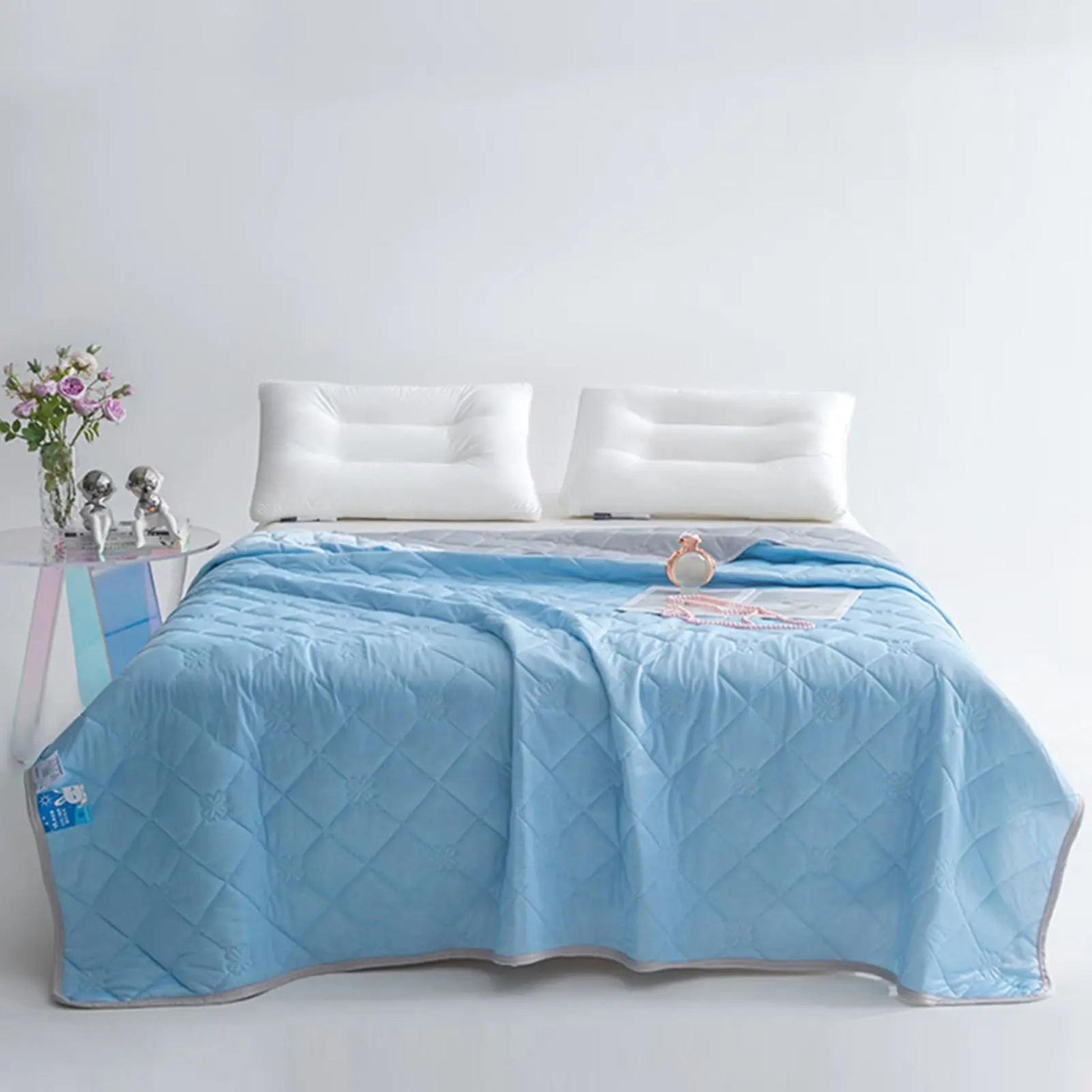 Light blue quilted cooling blanket with gray trim on a bed with white pillows.