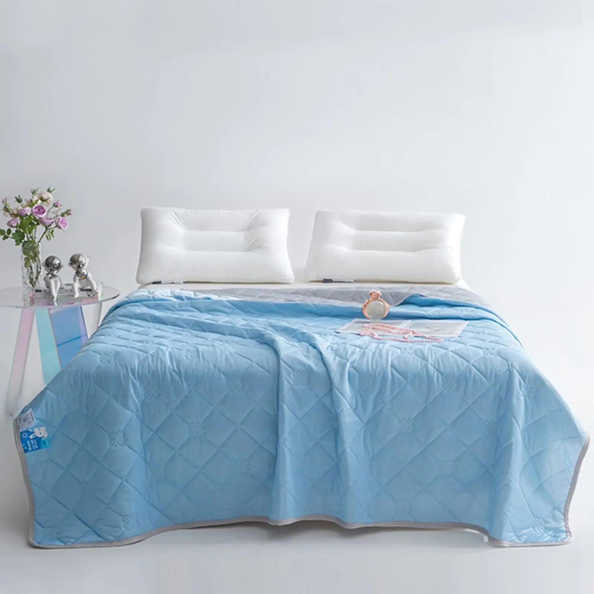 Light blue quilted cooling blanket with gray trim on a bed with white pillows.