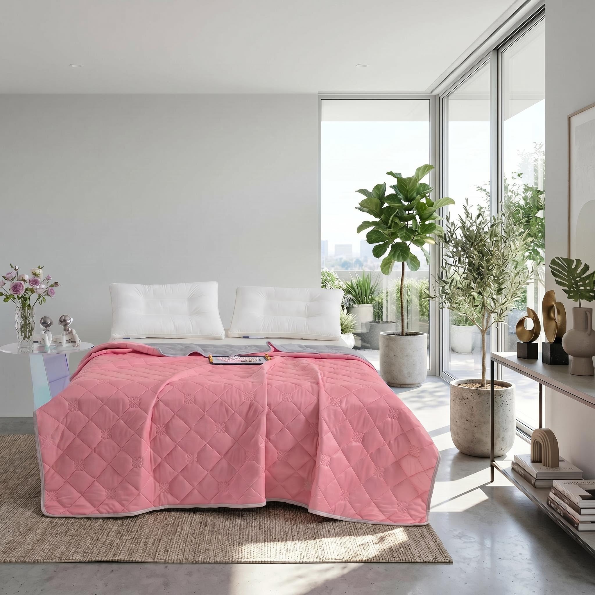 Pink quilted cooling blanket with a gray reverse side on a bed in a bright modern bedroom.