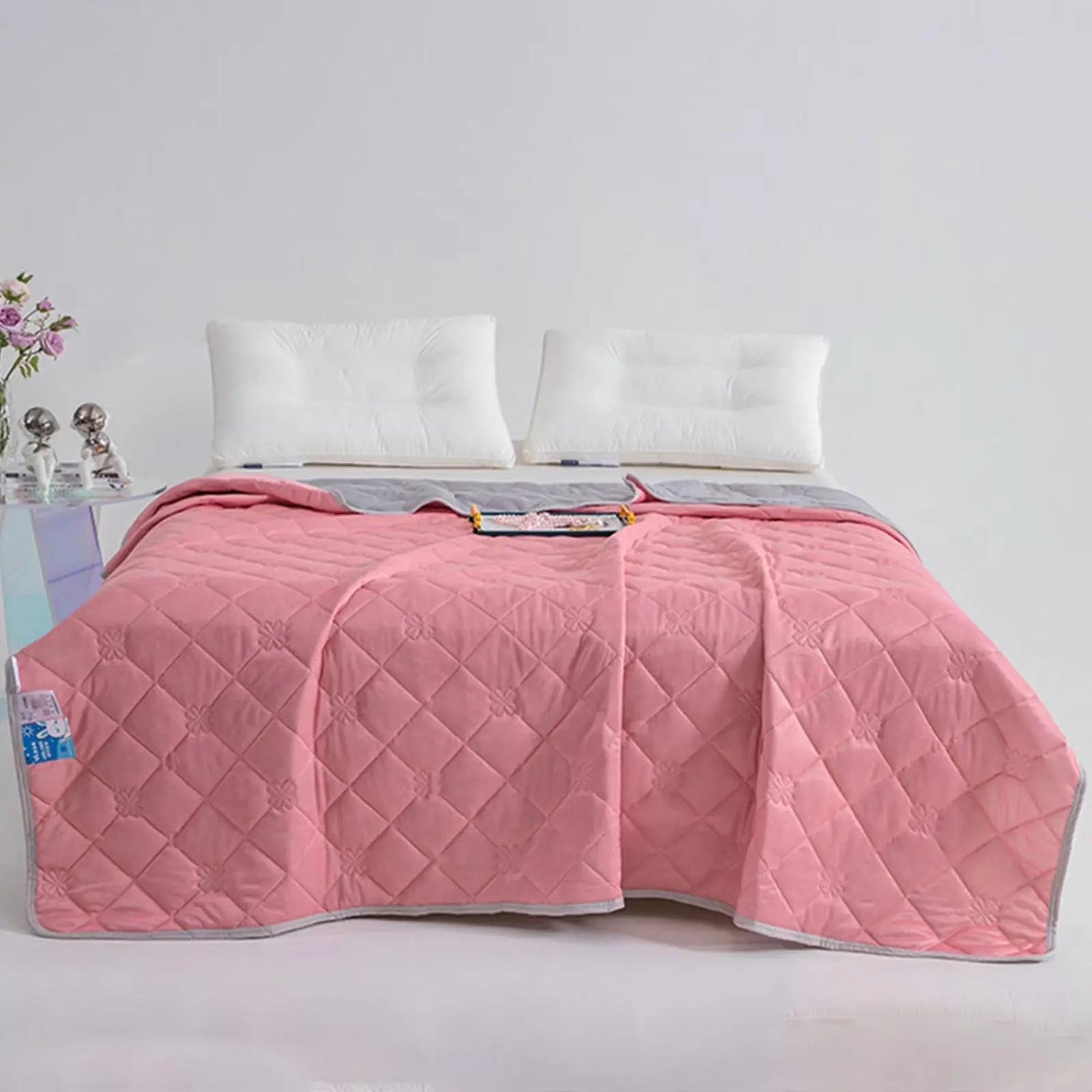Pink and gray reversible quilted cooling blanket on a bed with white pillows.