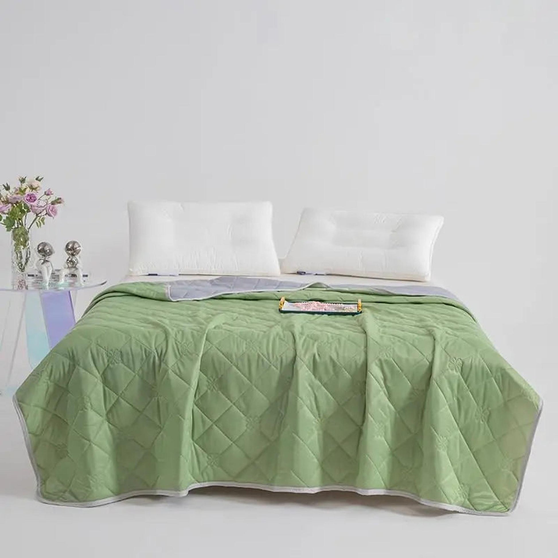 Light green quilted cooling blanket with a gray reversible side on a bed.