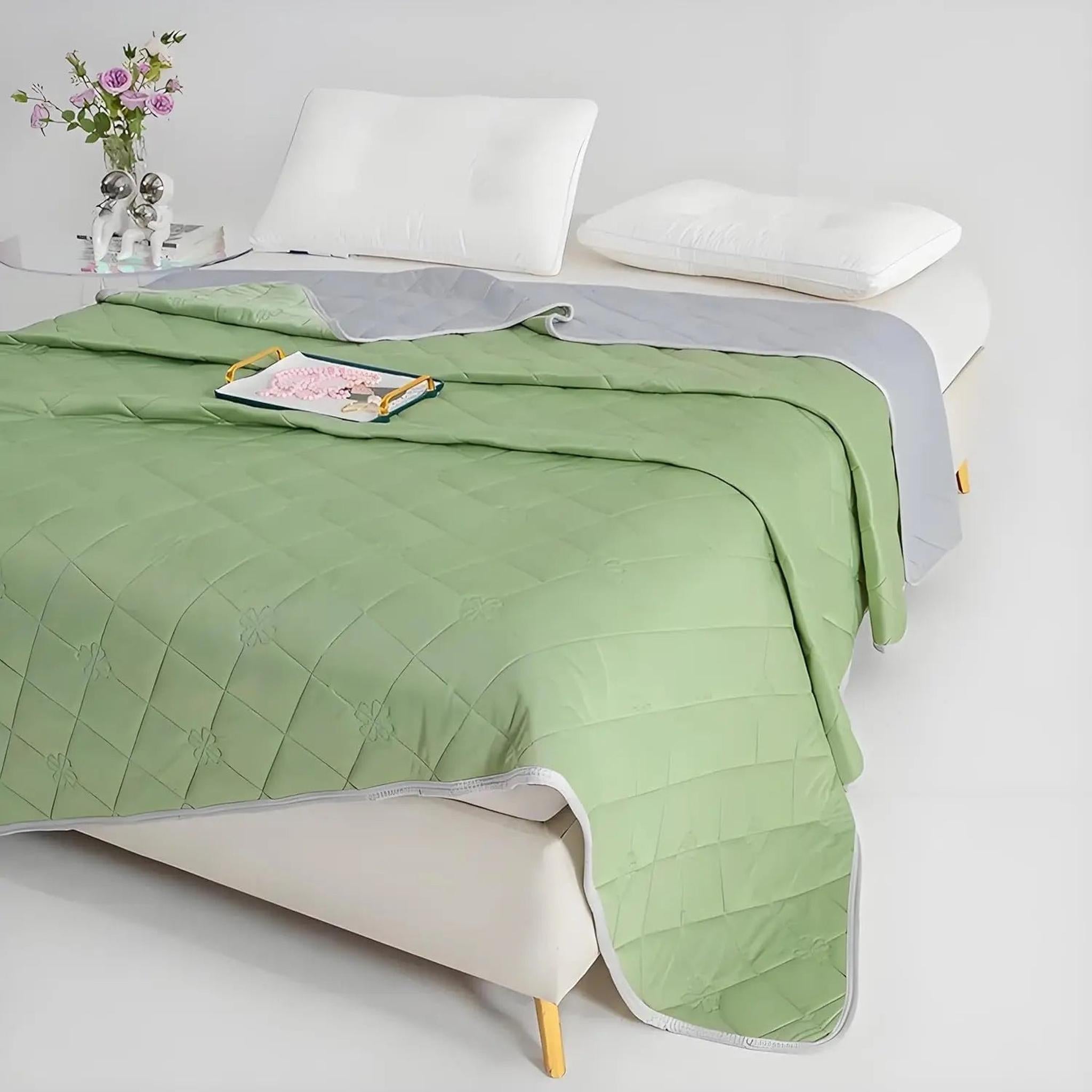 Green and gray reversible quilted polyester cooling blanket on a bed with white pillows.