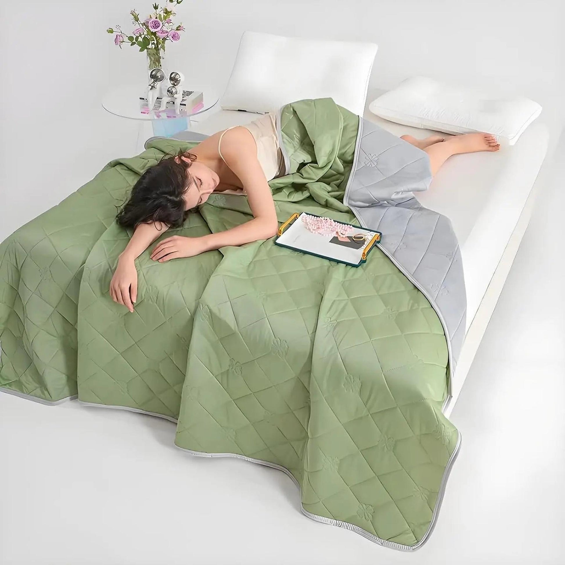 Woman sleeping under a green and gray reversible quilted cooling blanket on a white bed.