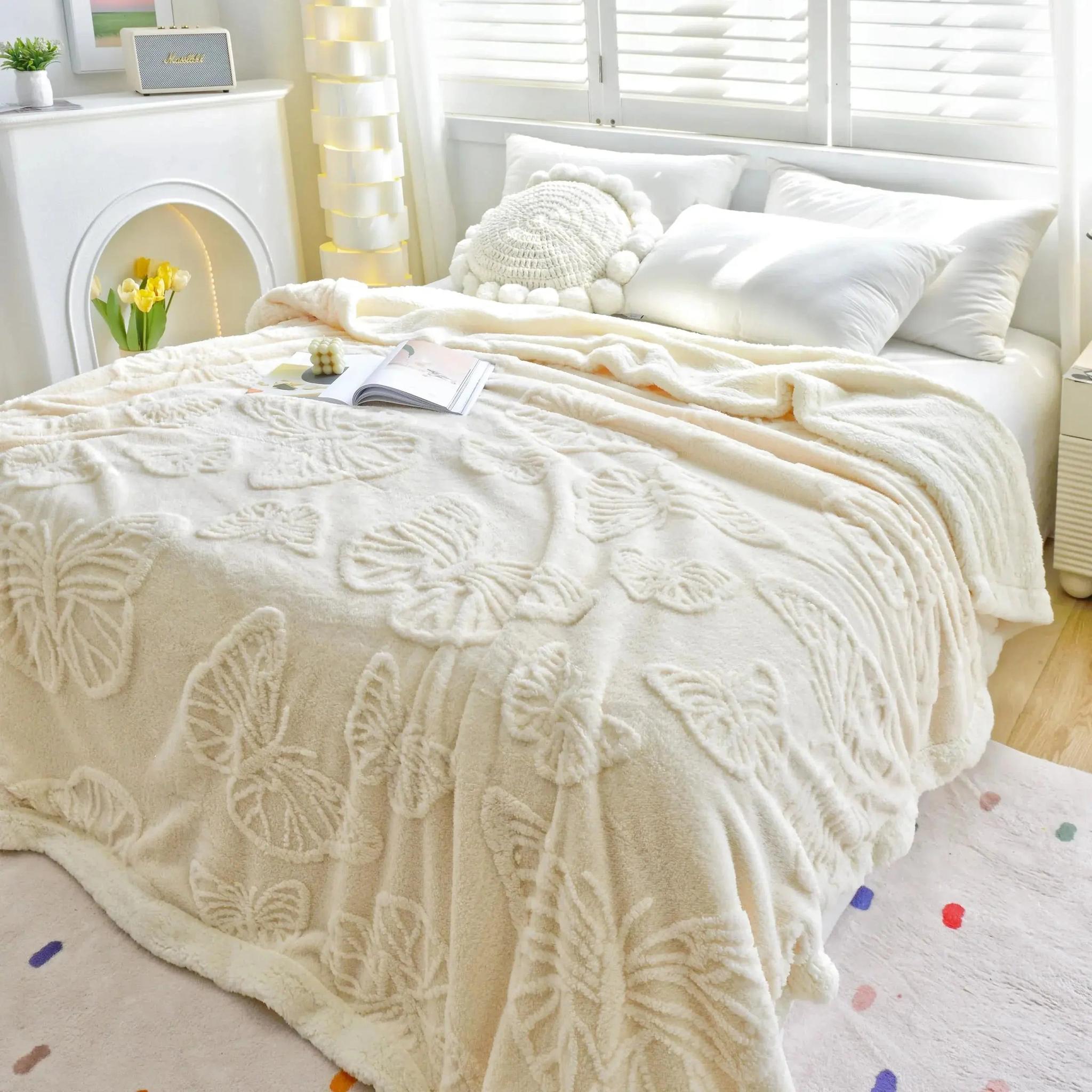 White coral fleece blanket with embossed butterfly design on a bed.