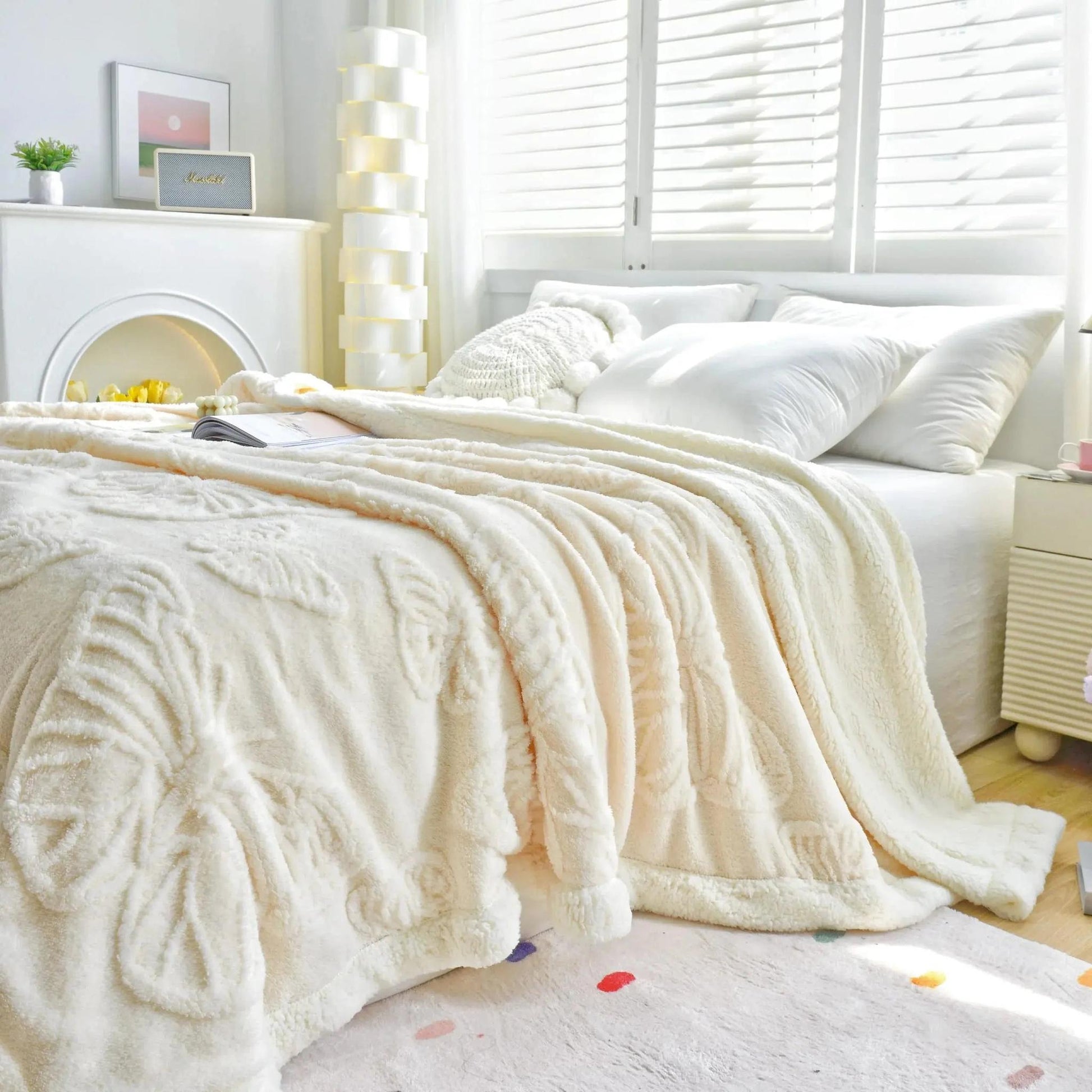 Cream coral fleece blanket with embossed butterfly charm design on a bed.