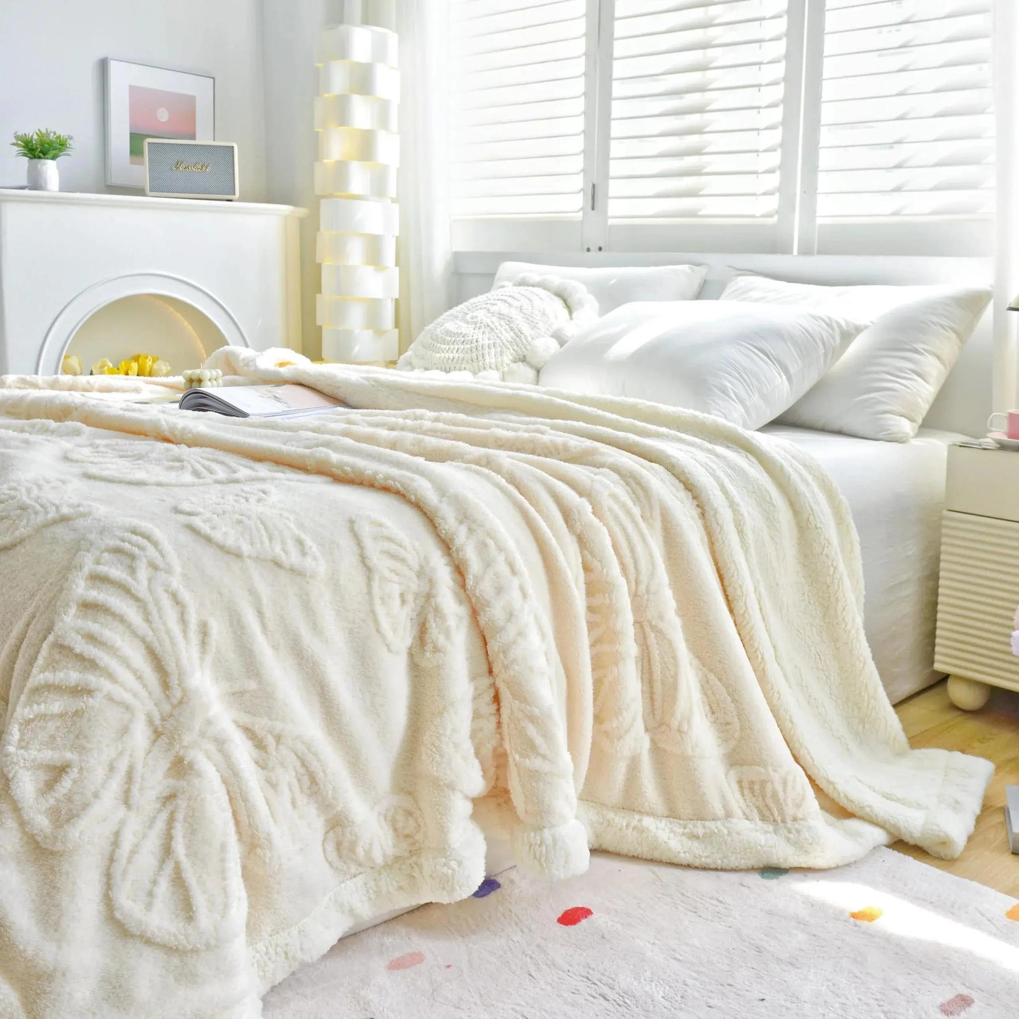 Cream coral fleece blanket with embossed butterfly charm design on a bed.