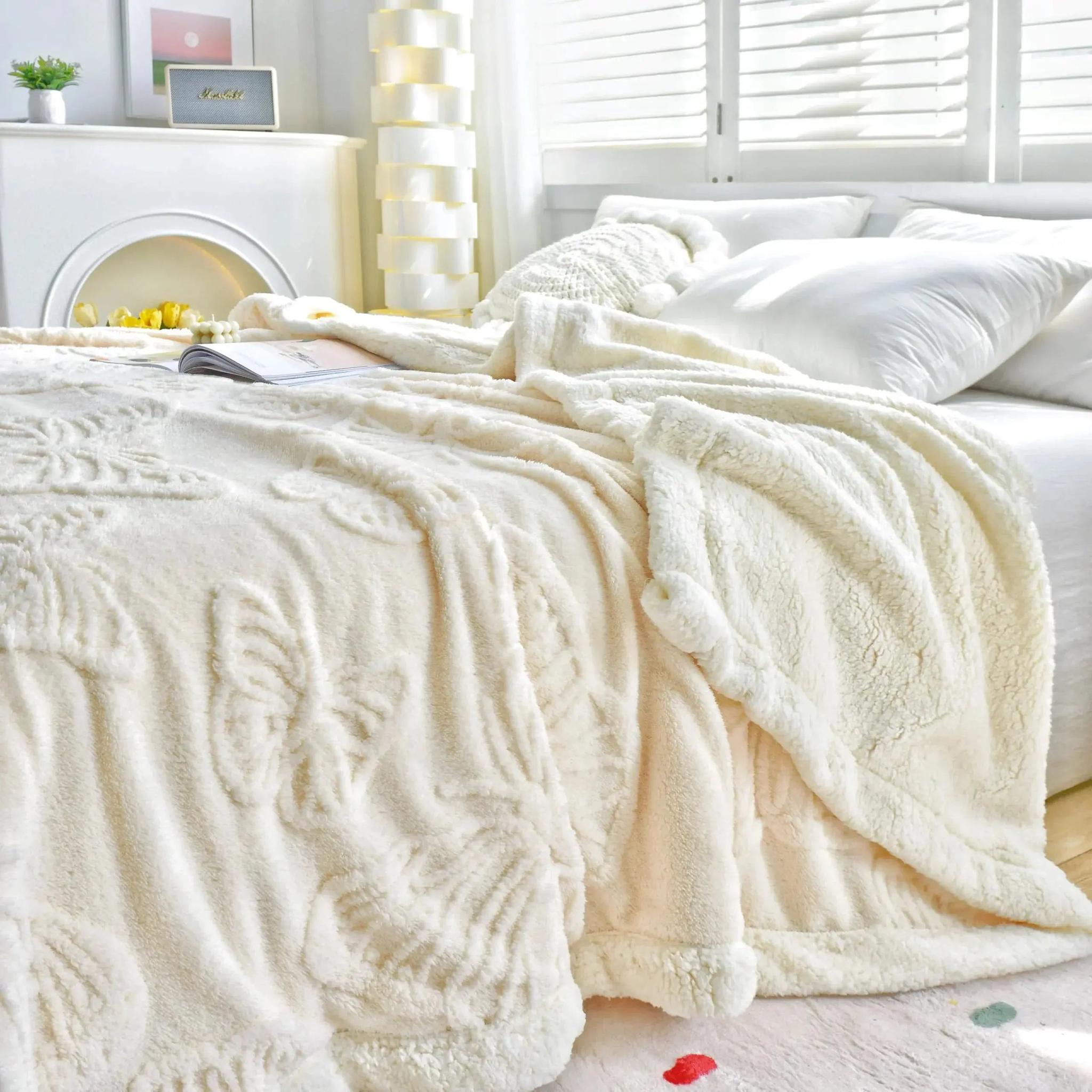 Cream coral fleece blanket with embossed butterfly and floral designs draped on a bed.