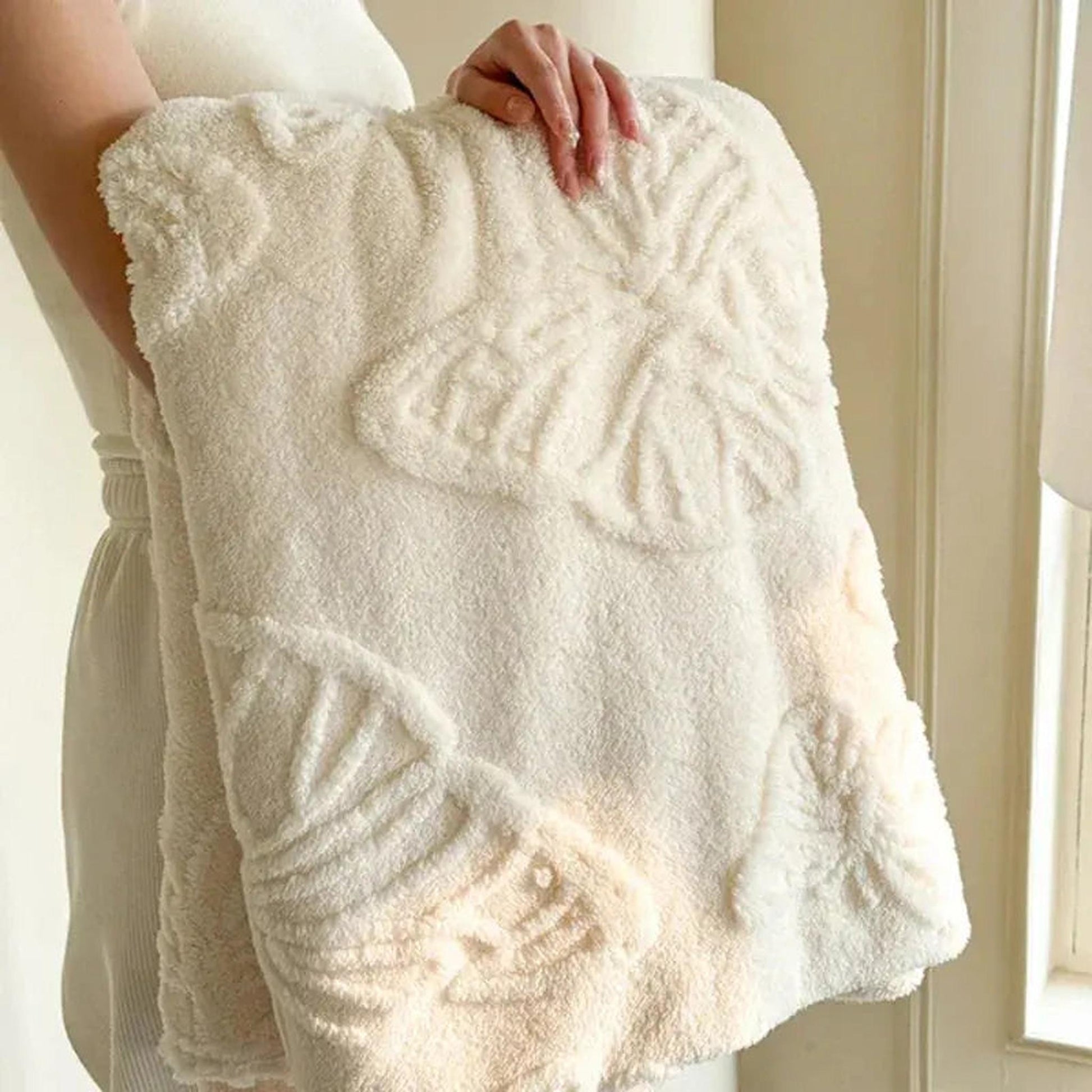 White coral fleece blanket with raised butterfly charm design, held by a person.