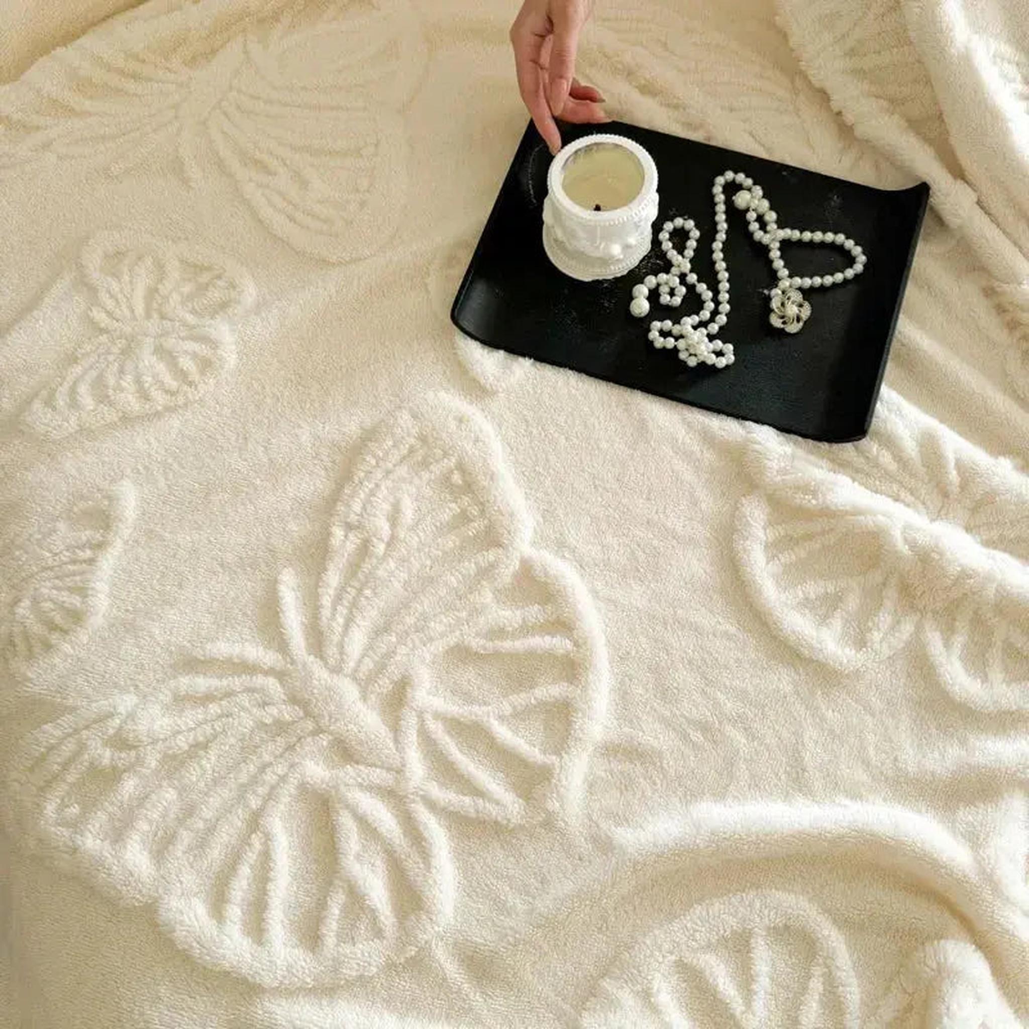 White coral fleece blanket with embossed butterfly charm design, a hand holding a candle, and pearl necklace on a tray.