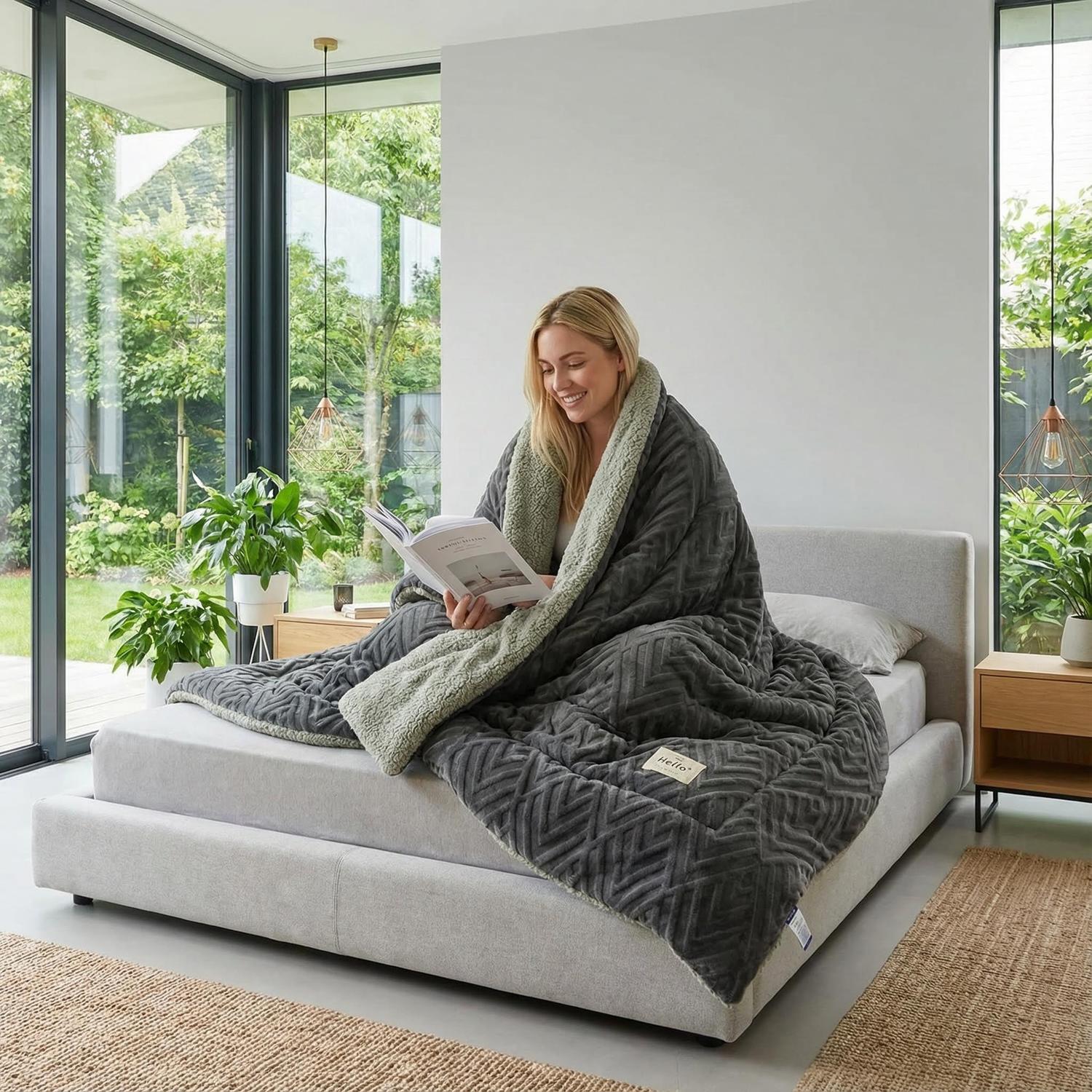Woman on bed wrapped in a deep gray coral fleece weighted blanket with a soft lambswool lining.