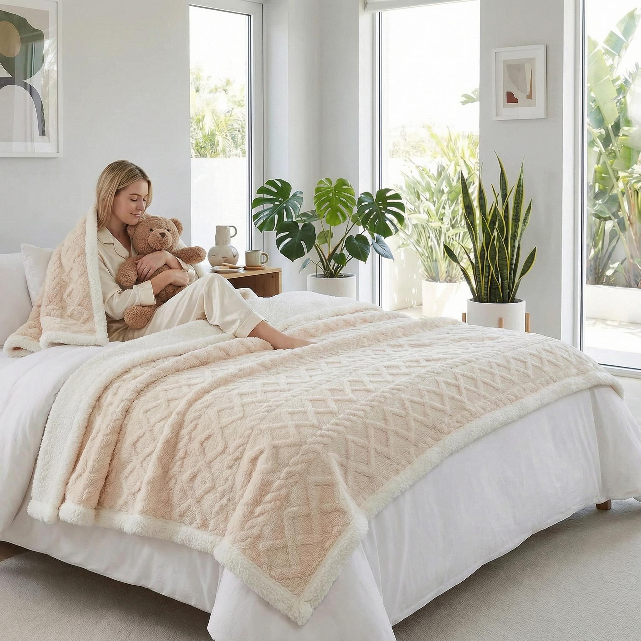 Woman on bed with a reversible coral velvet blanket, featuring a cream cable knit pattern and soft sherpa lining.