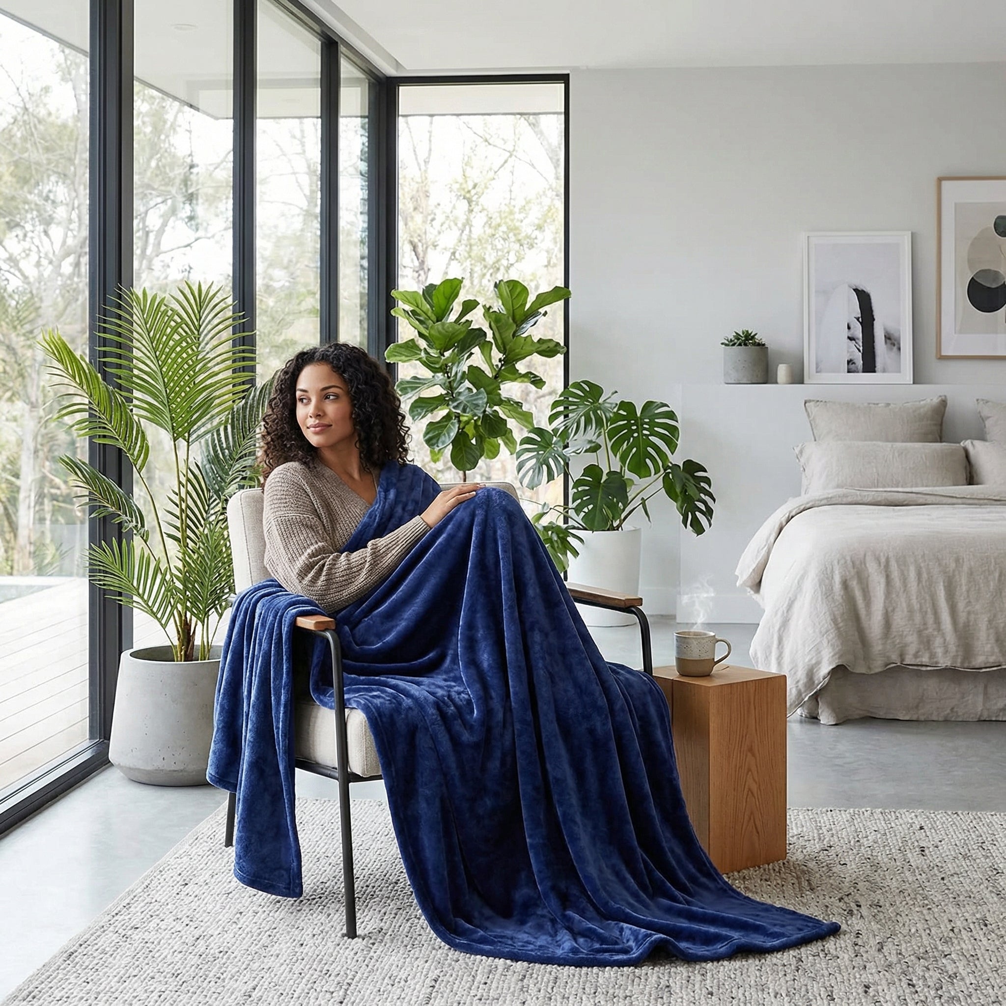 Woman relaxing in a modern living room, wrapped in a plush navy blue coral velvet throw blanket.
