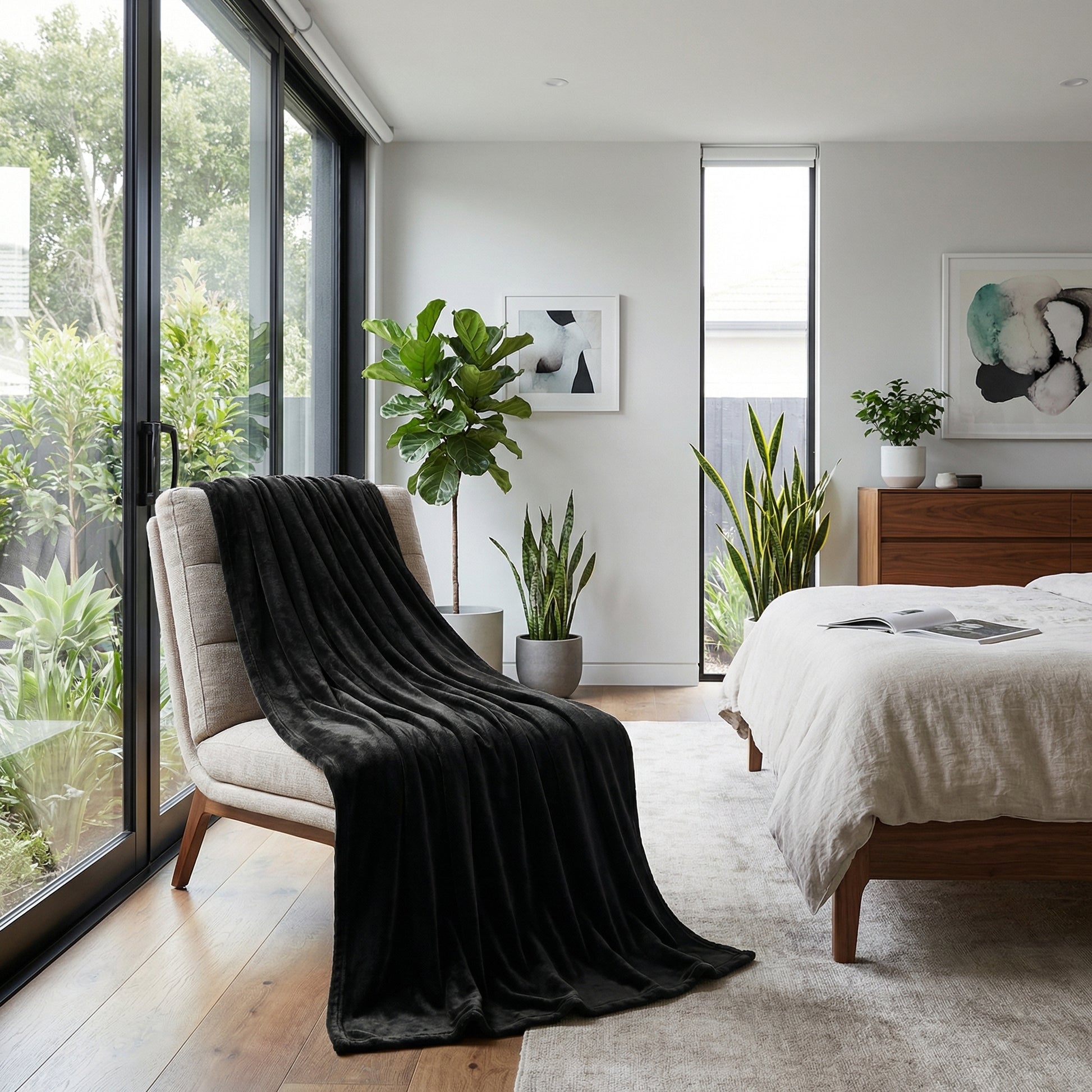 Black coral velvet throw blanket draped over a beige armchair in a bright, modern bedroom.
