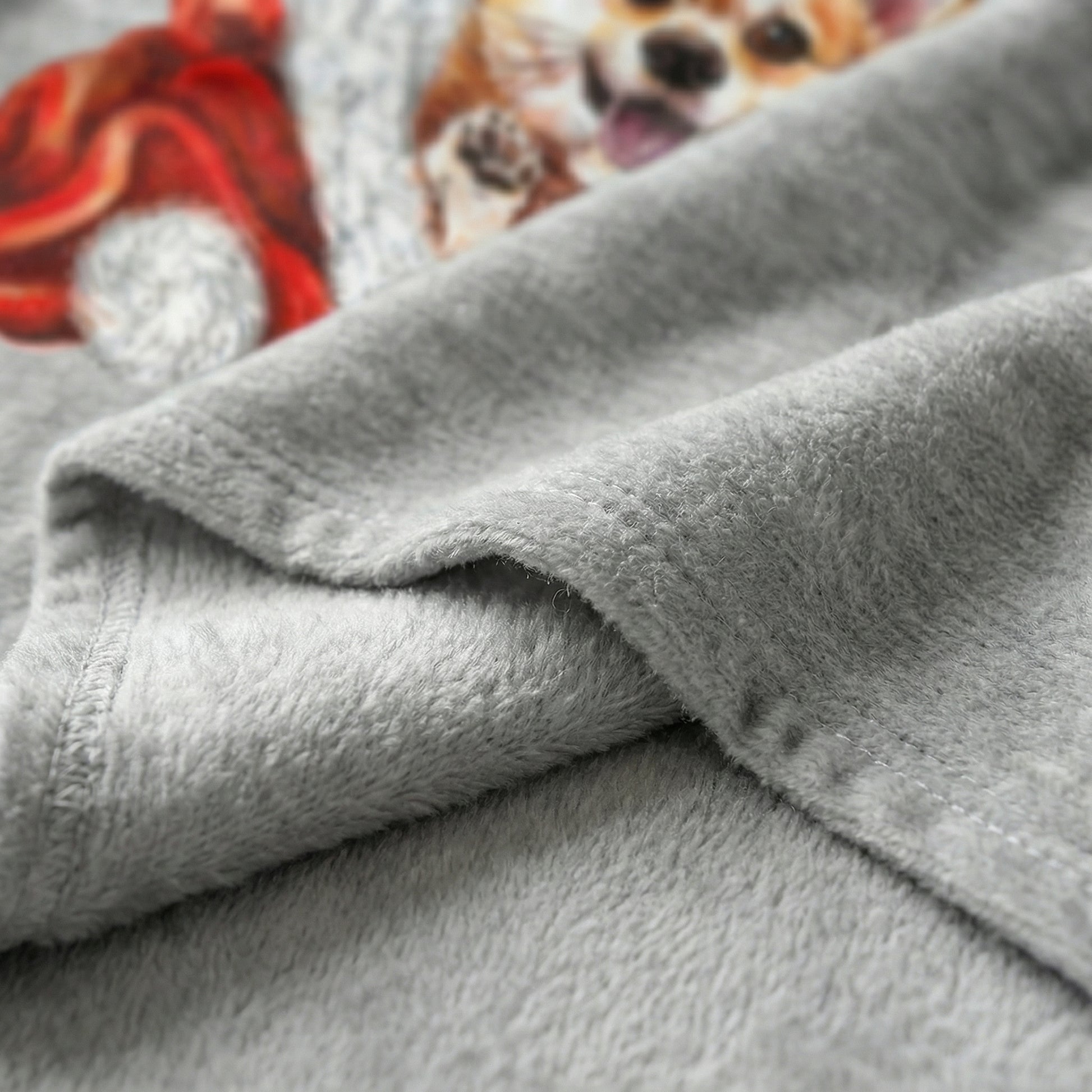Close-up of a soft, gray flannel blanket with a playful Corgi print and a red winter hat.