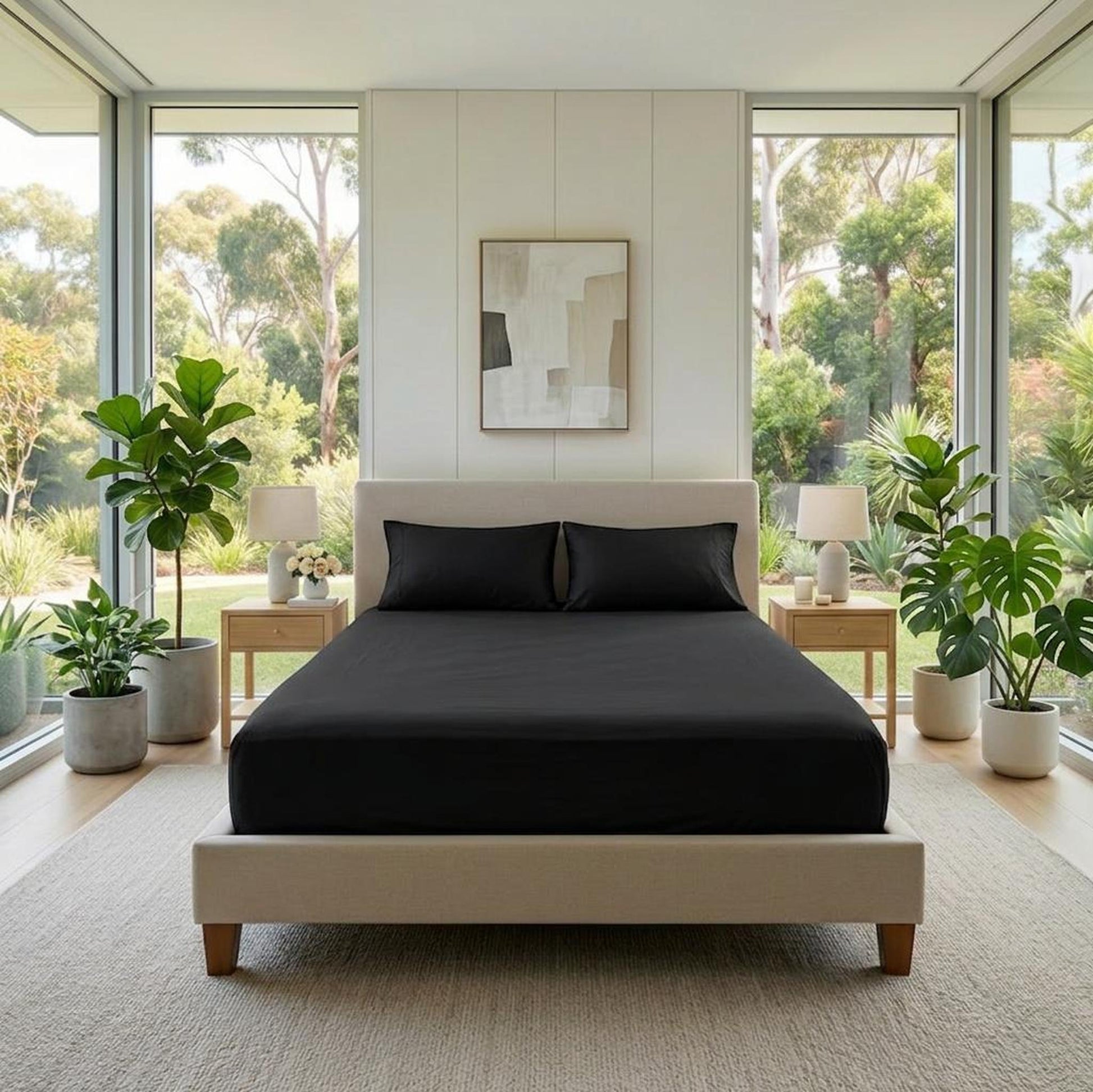 Black cotton fitted sheet on a bed with two pillows, in a bright bedroom with large windows.