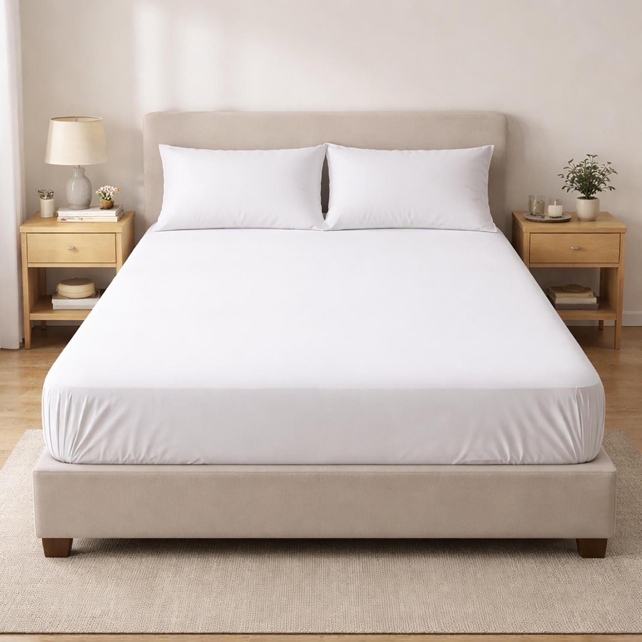 White cotton fitted sheet on a bed with two pillows, showcasing its snug fit and soft texture.