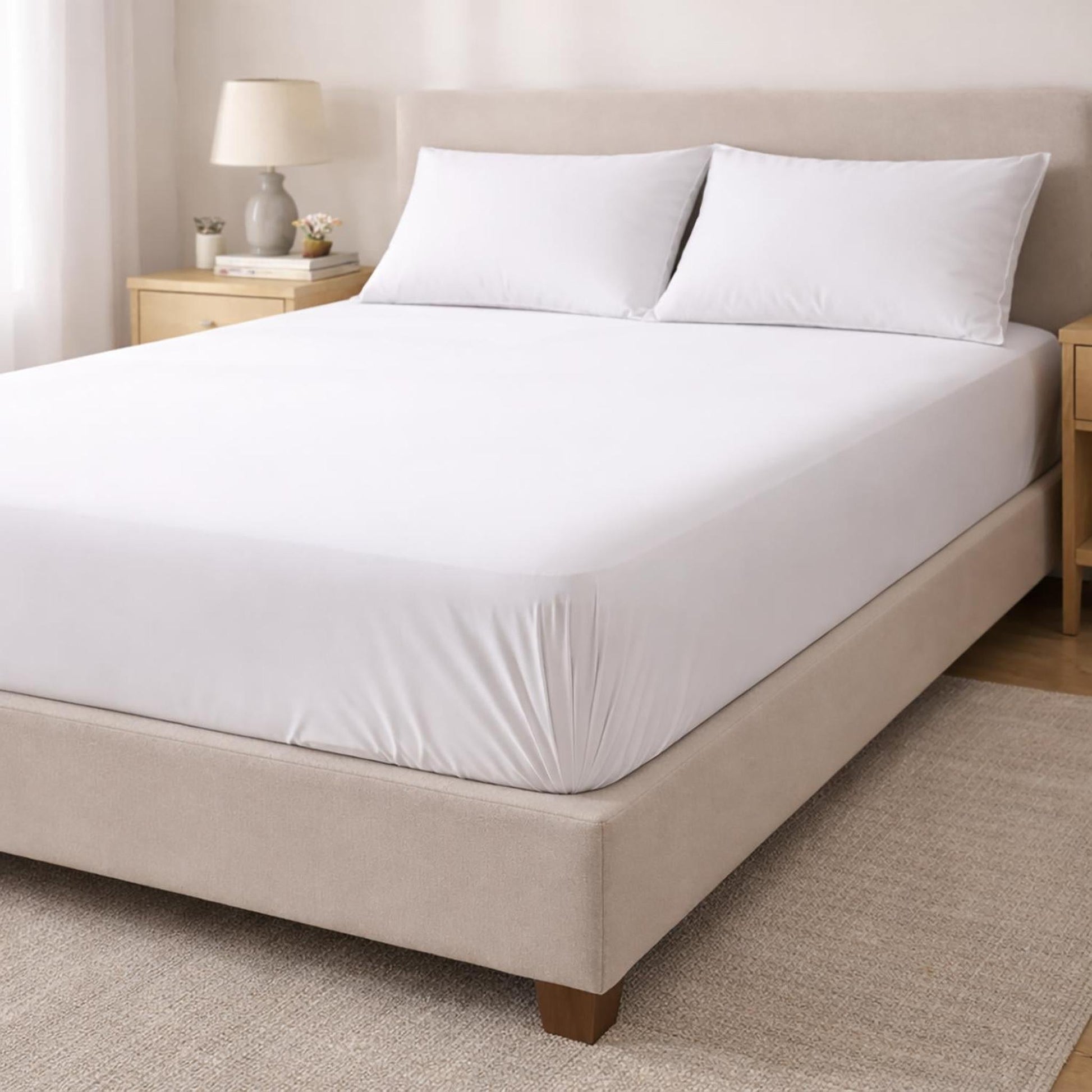 White cotton fitted sheet on a bed with two pillows, showcasing its snug fit and soft texture.