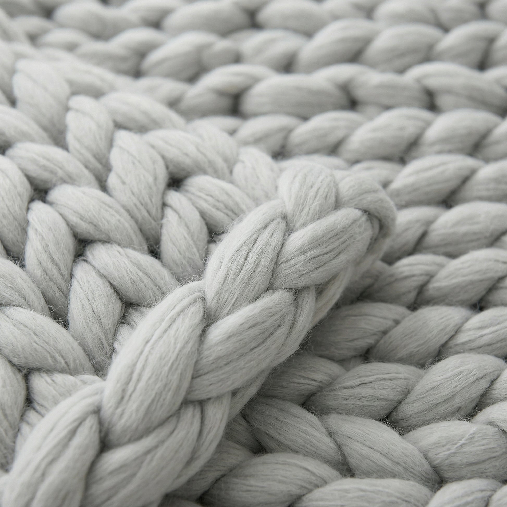 Close-up of a soft, light gray chunky knit blanket with visible wool texture.