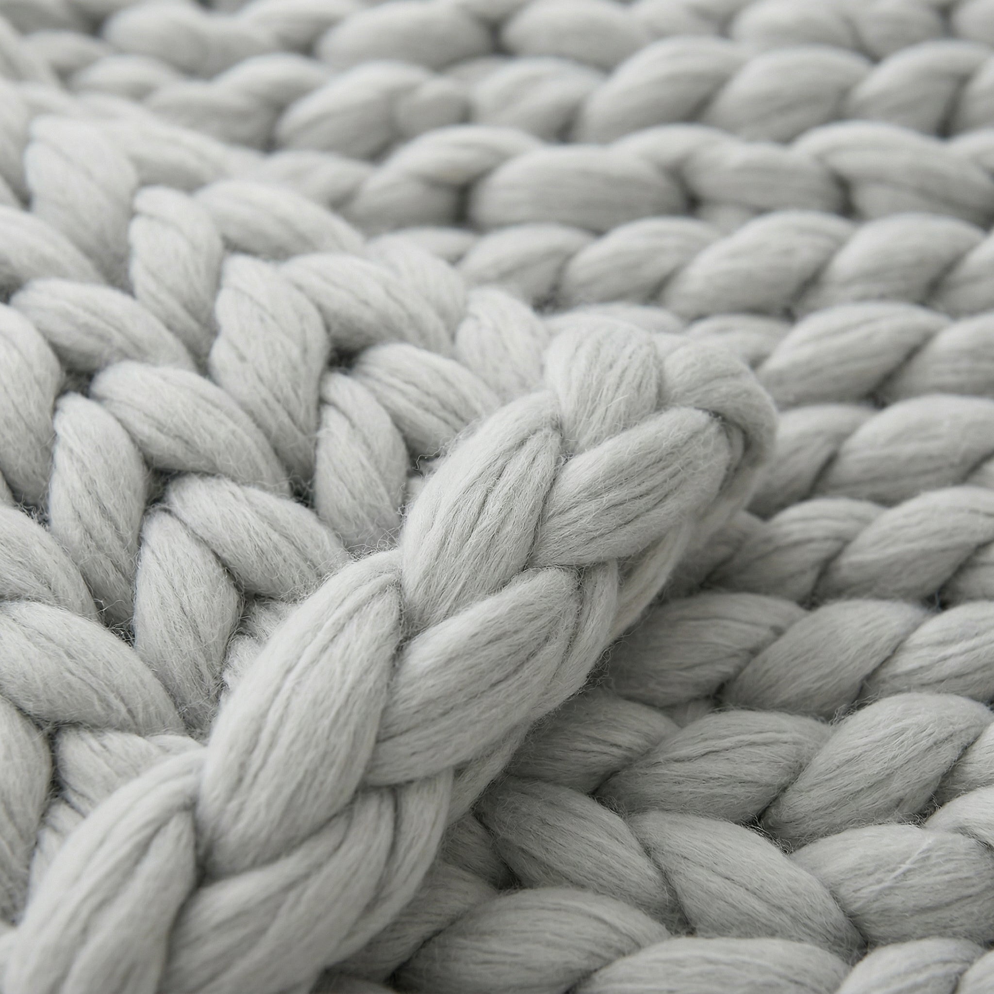 Close-up of a soft, light gray chunky knit blanket with visible wool texture.