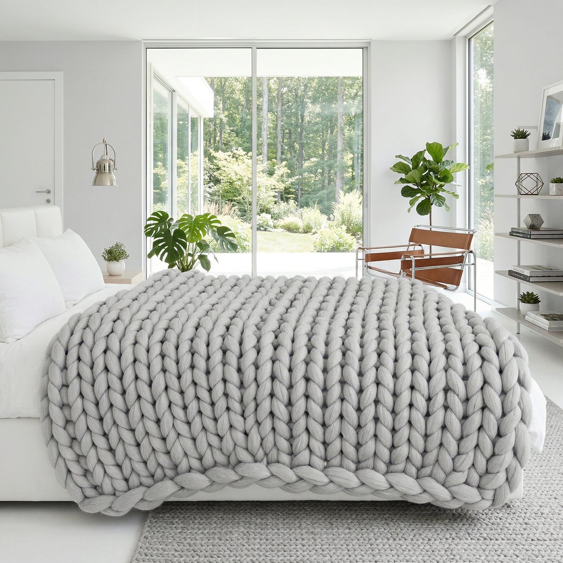 Light gray chunky knit blanket on a white bed in a modern, bright bedroom with large windows.