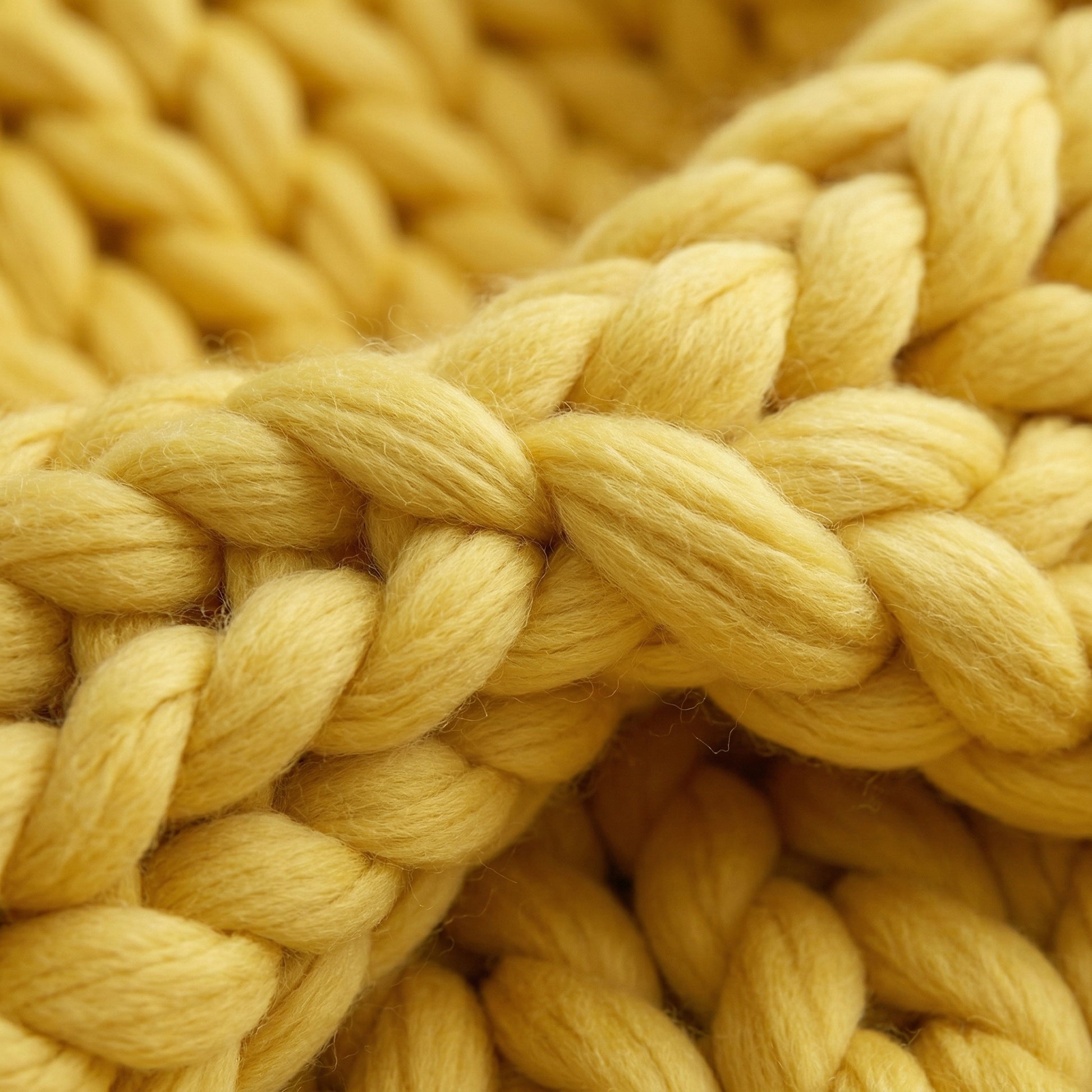 Close-up of a soft, chunky knit blanket in a vibrant yellow, showcasing its woven texture.