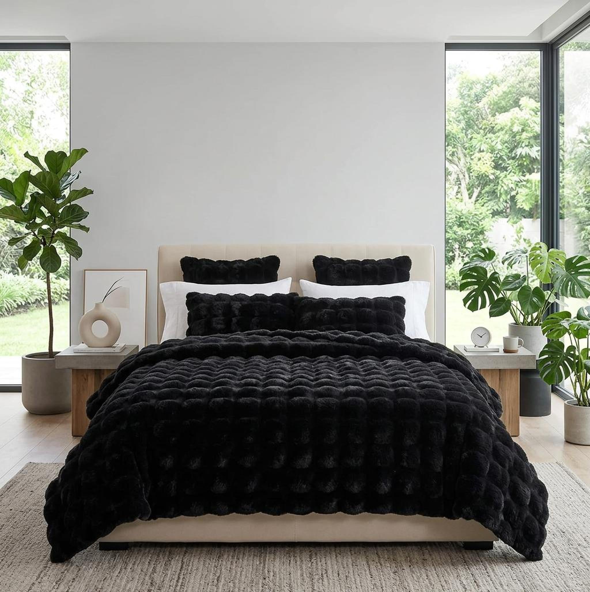 Plush black faux rabbit fleece throw blanket on a bed with matching pillows in a bright room.