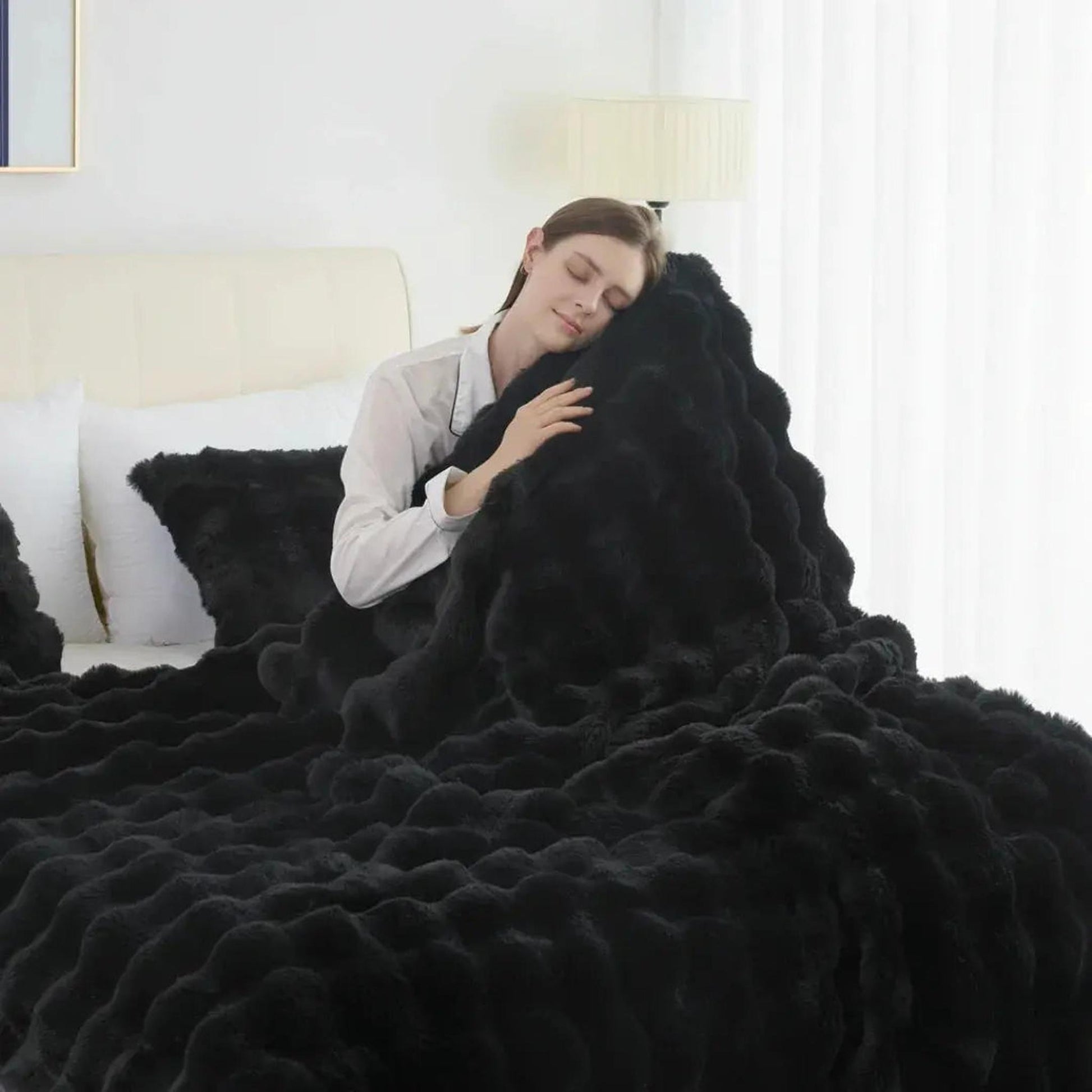 Woman sleeping peacefully under a plush, black faux rabbit fleece throw blanket with a wavy texture.