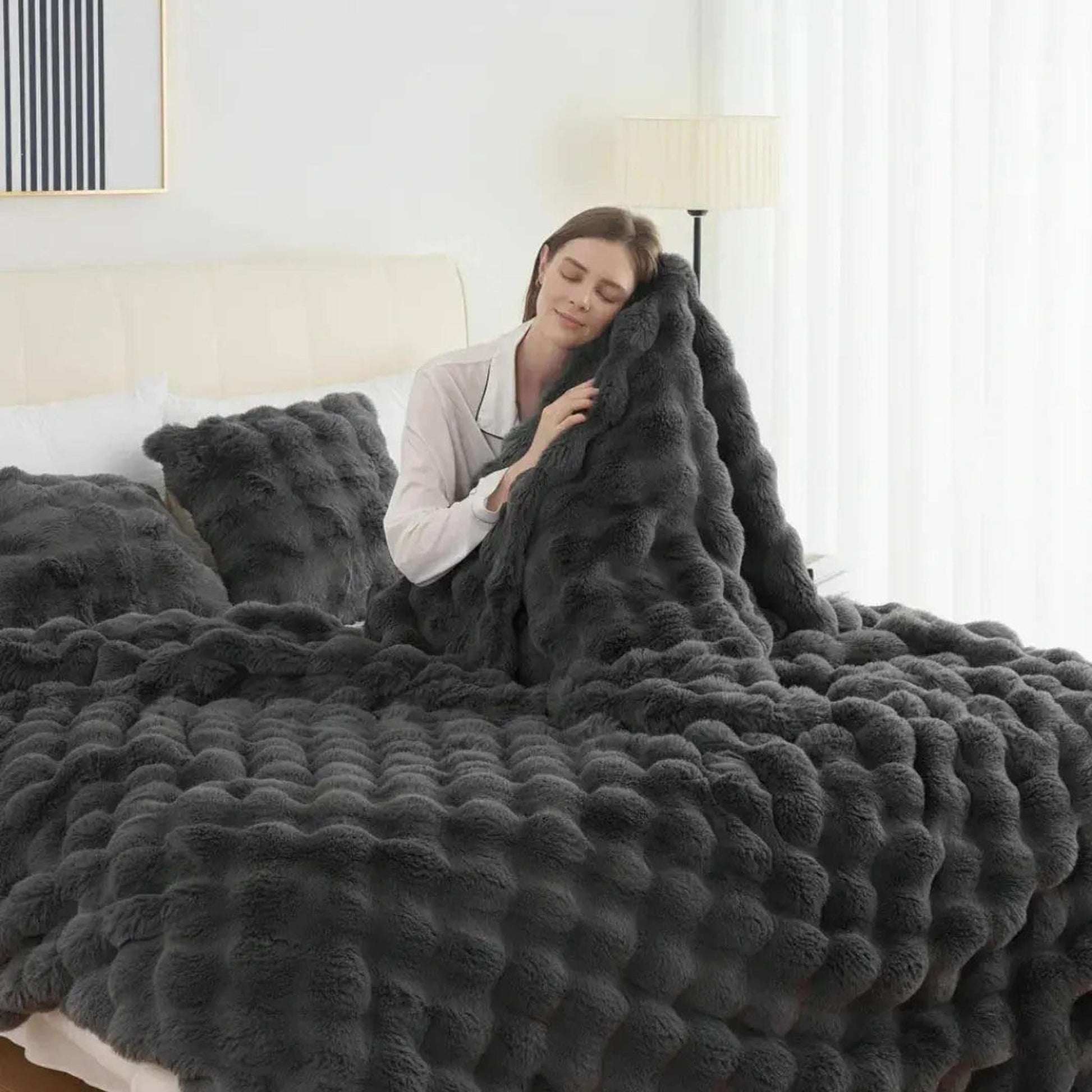 Woman snuggled in a dark gray faux rabbit fleece throw blanket with a textured bubble pattern.