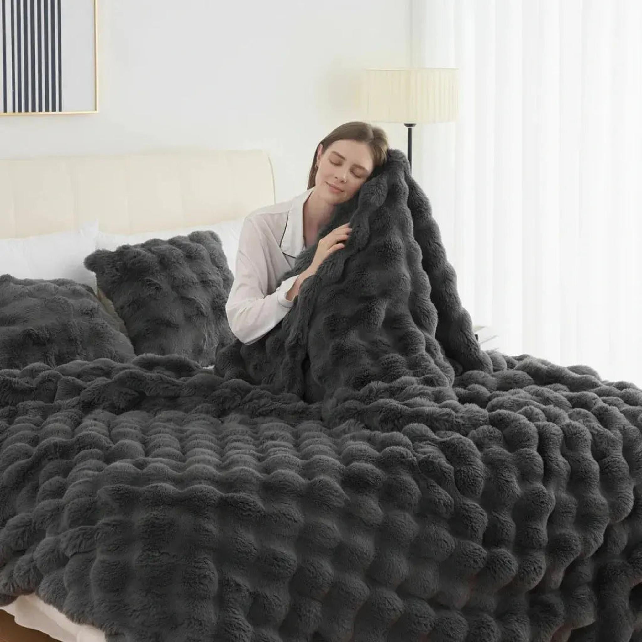 Woman snuggled in a dark gray faux rabbit fleece throw blanket with a textured bubble pattern.