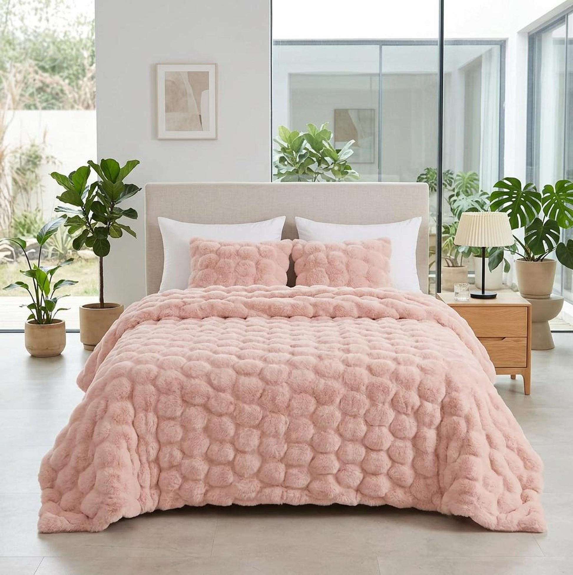 Pink faux rabbit fleece throw blanket with a textured bubble pattern on a bed with white pillows.
