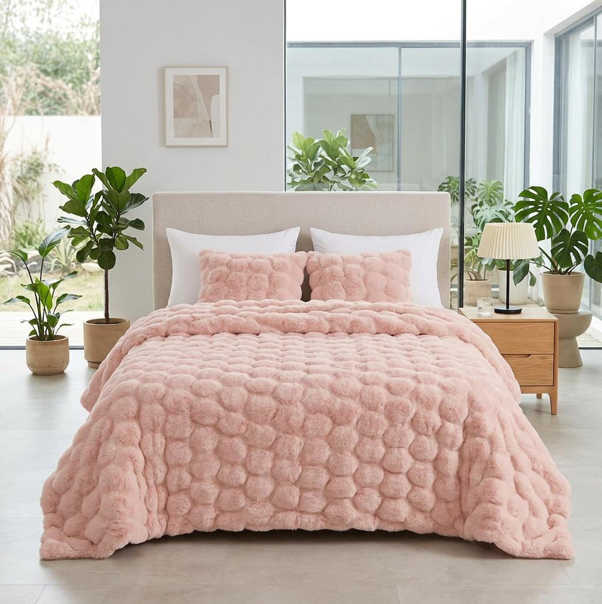 Pink faux rabbit fleece throw blanket with a textured bubble pattern on a bed with white pillows.