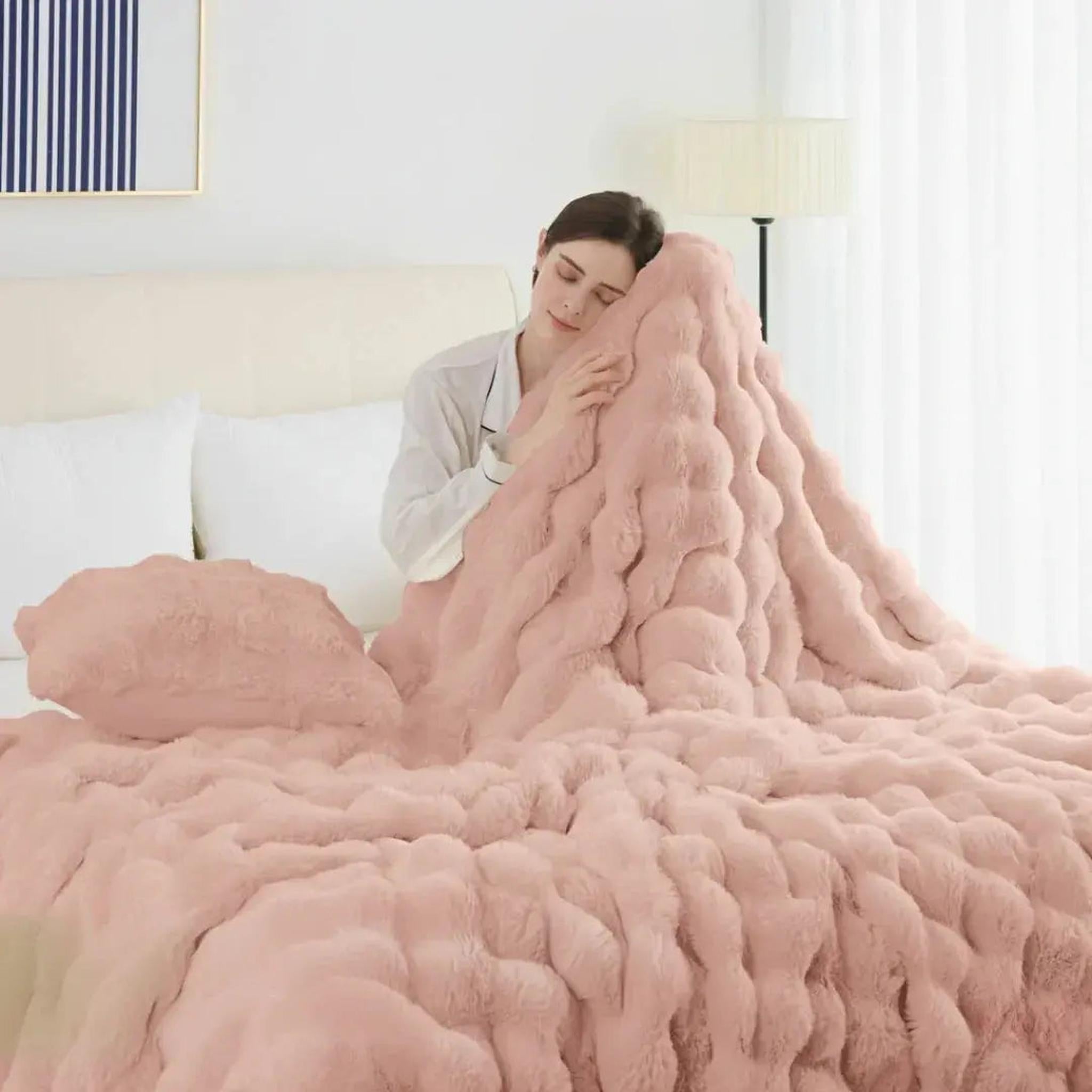 Woman snuggling a plush pink faux rabbit fleece throw blanket on a bed.