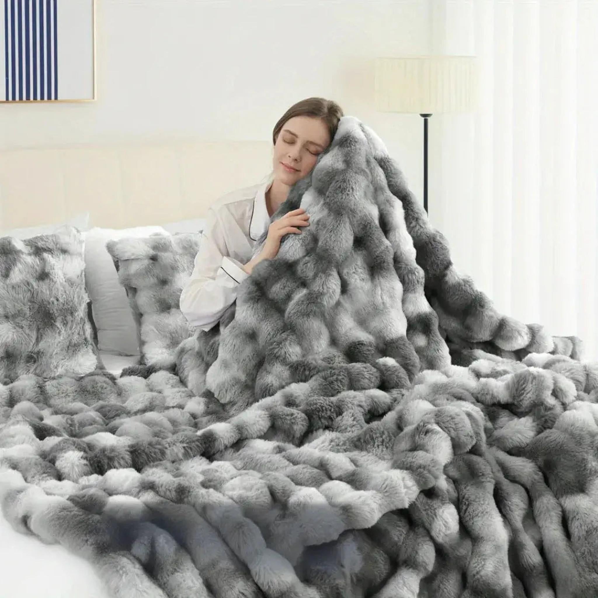 Woman in bed cuddling a plush gray faux rabbit fleece throw blanket and matching pillows.