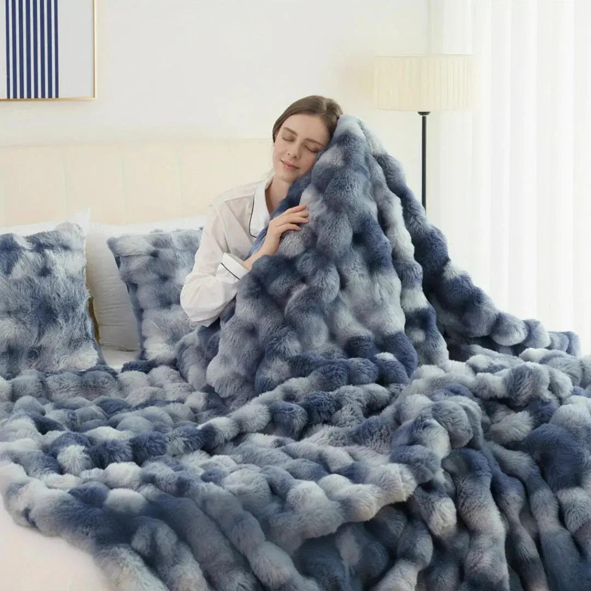 Woman relaxing in bed with a cozy blue and white faux rabbit fleece throw blanket and matching pillows.