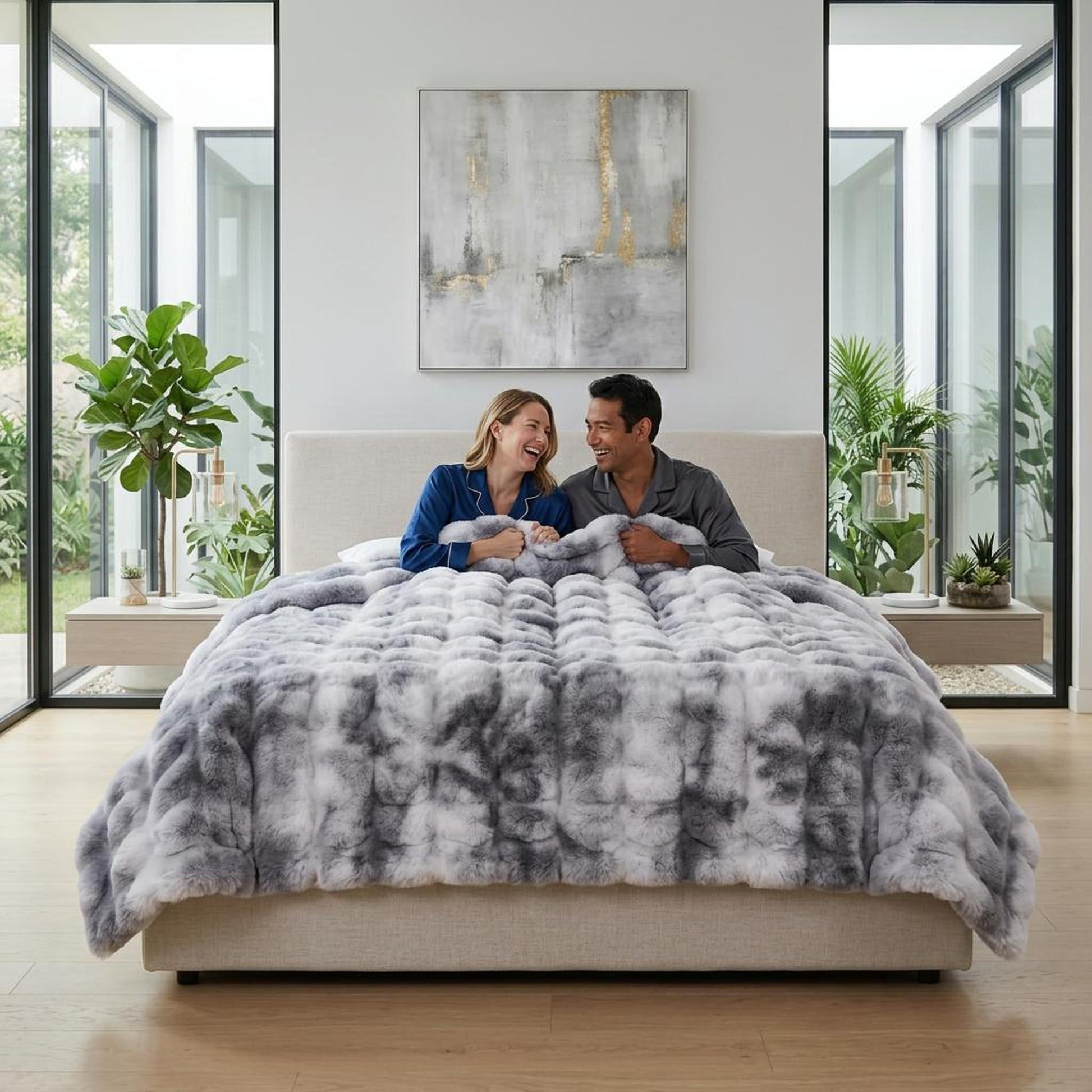 Couple laughing under a gray and white faux rabbit fleece throw blanket on a bed.