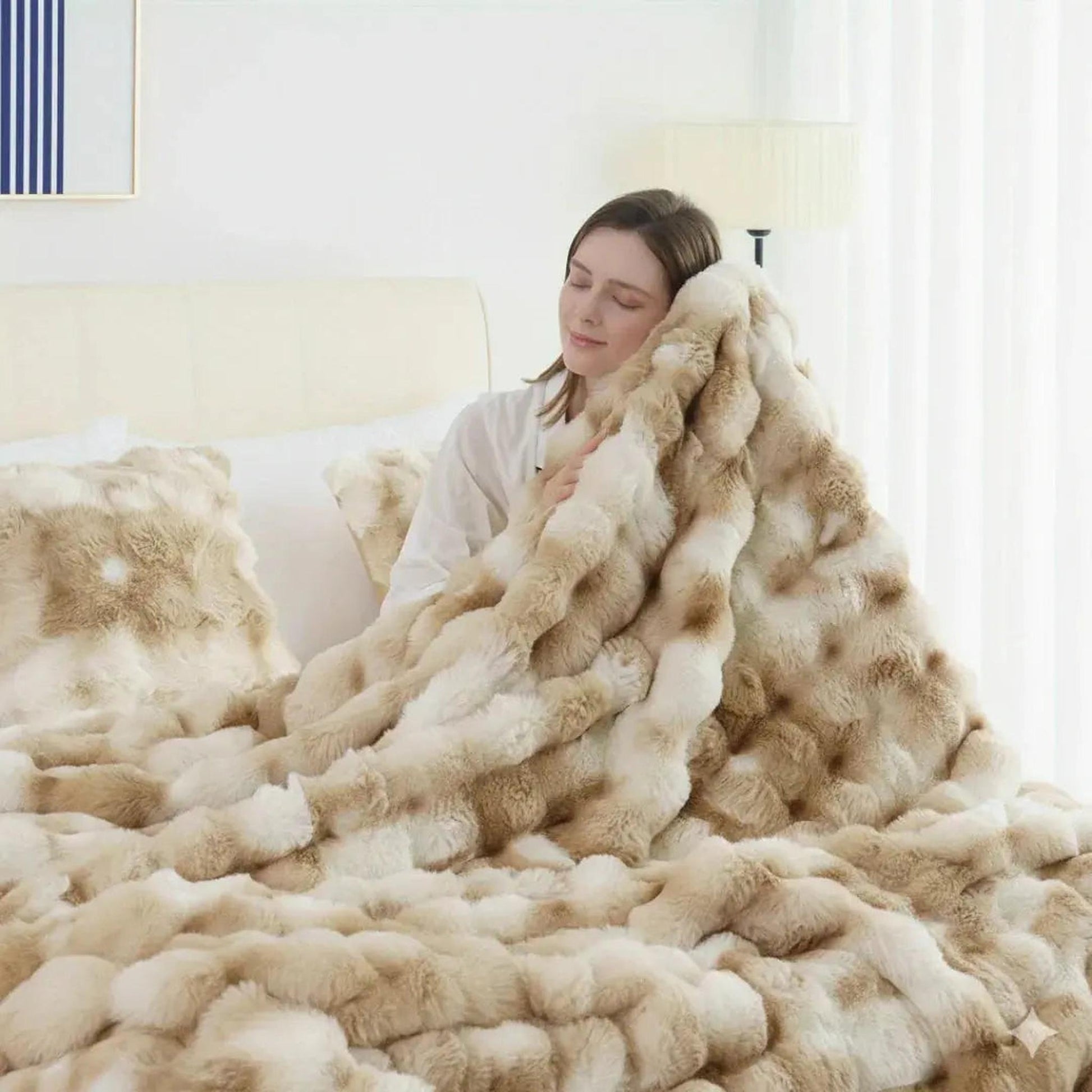 Woman snuggled in a plush, reversible faux rabbit fleece throw blanket in shades of cream and brown.
