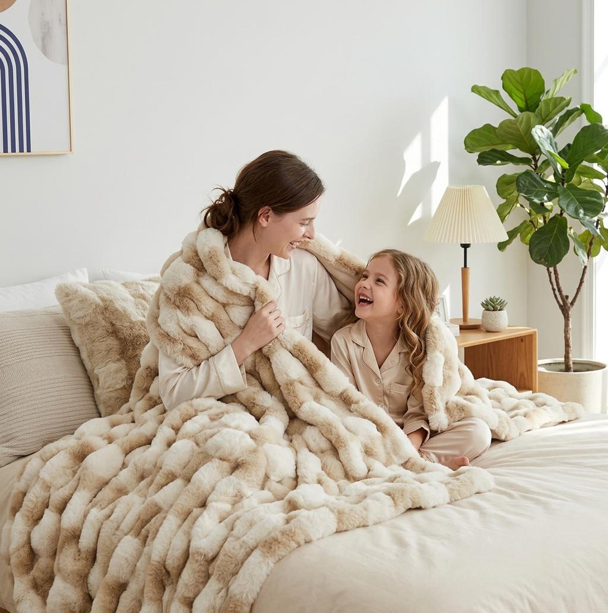 Smiling mother and child wrapped in a cozy beige faux rabbit fleece throw blanket on a bed.
