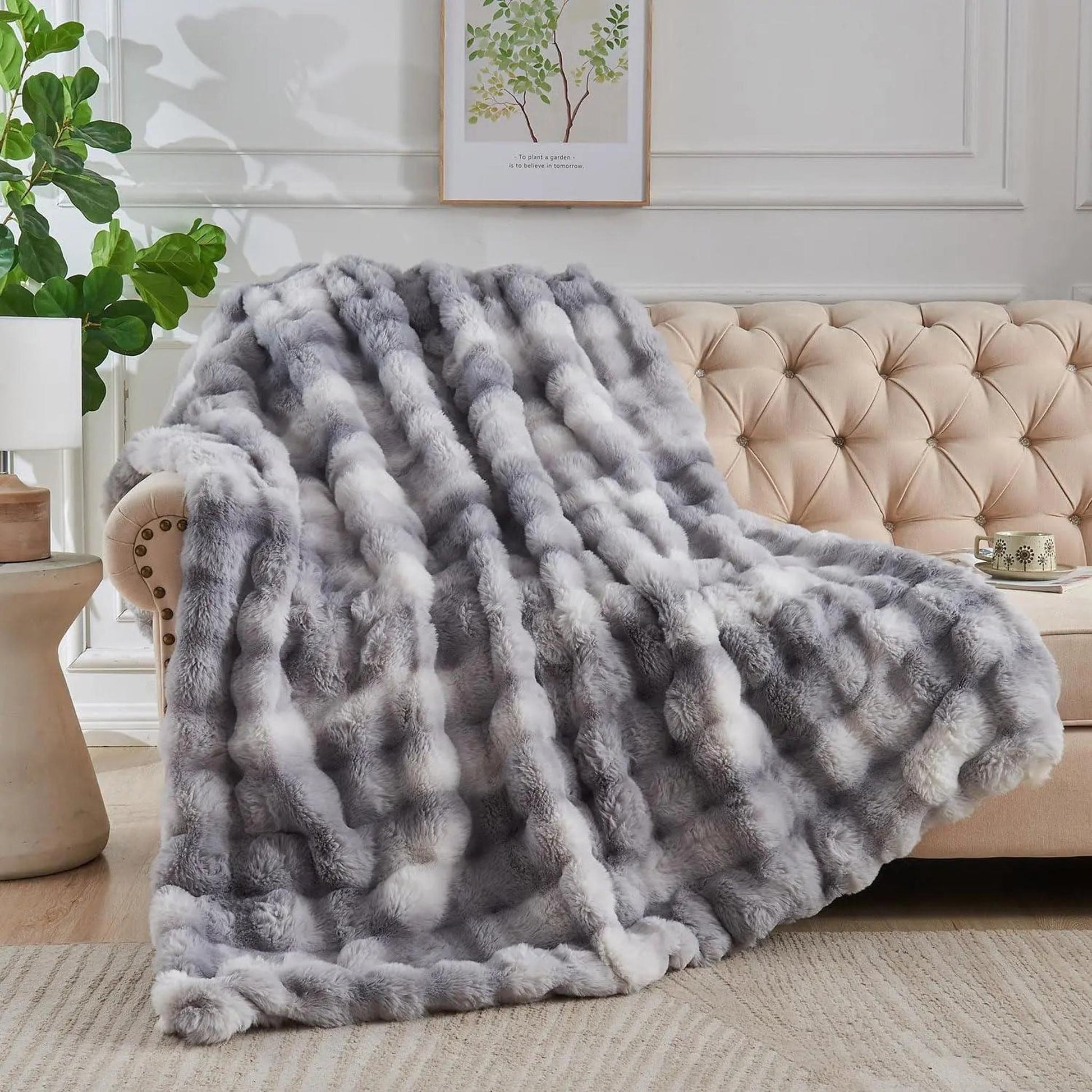 Gray and white faux rabbit fleece throw blanket draped over a beige tufted sofa.