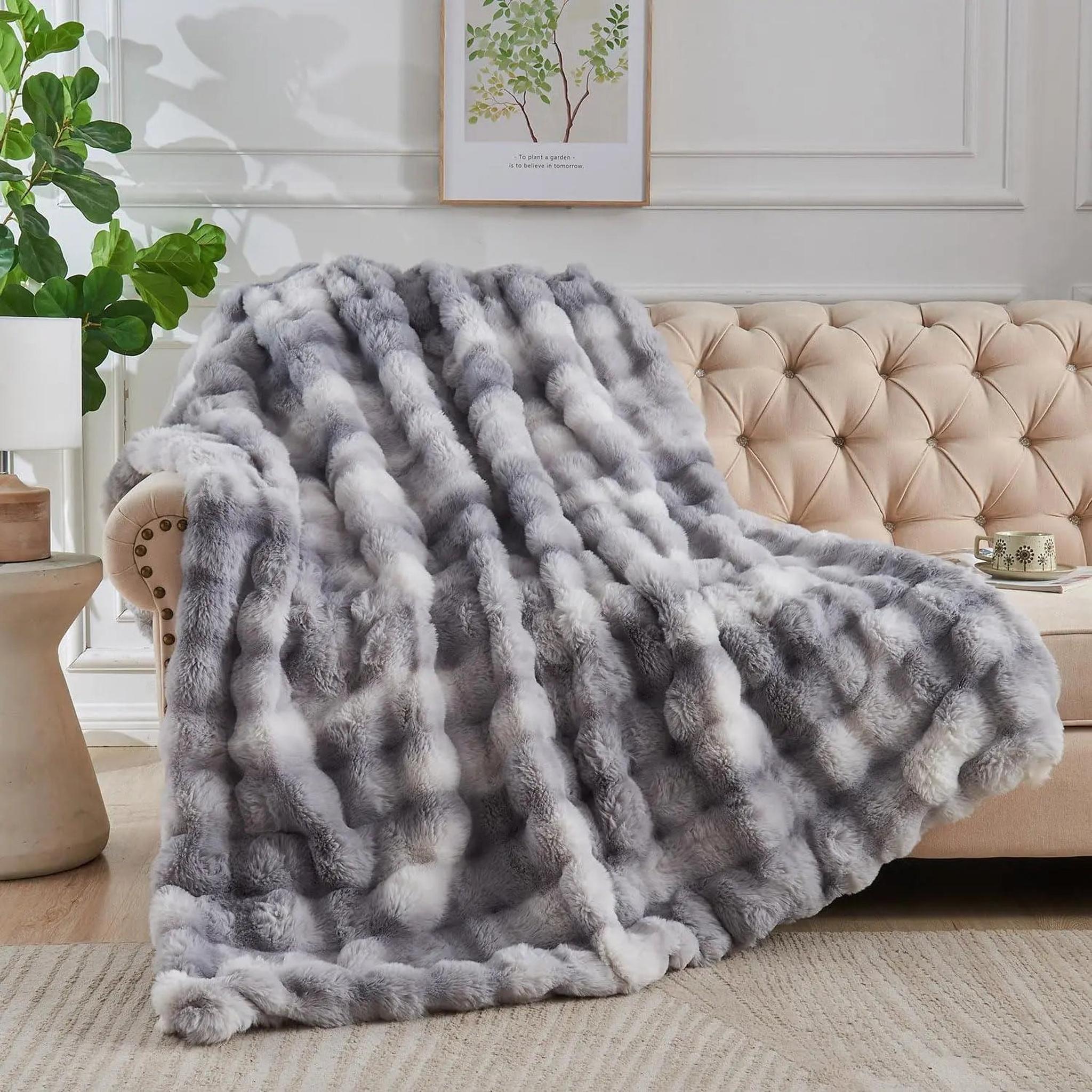 Gray and white faux rabbit fleece throw blanket draped over a beige tufted sofa.