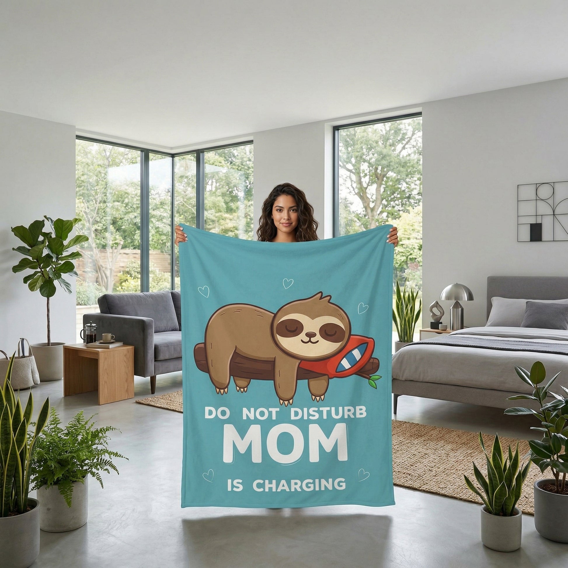 Woman holding a turquoise flannel throw blanket with a sleeping sloth and "DO NOT DISTURB MOM IS CHARGING" text.