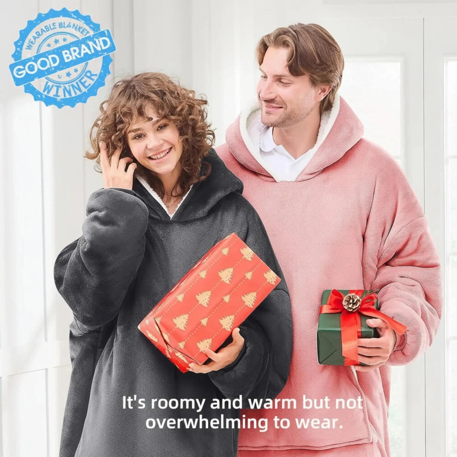 Smiling couple in oversized, cozy fleece hooded jackets, one charcoal and one pink, holding gifts.