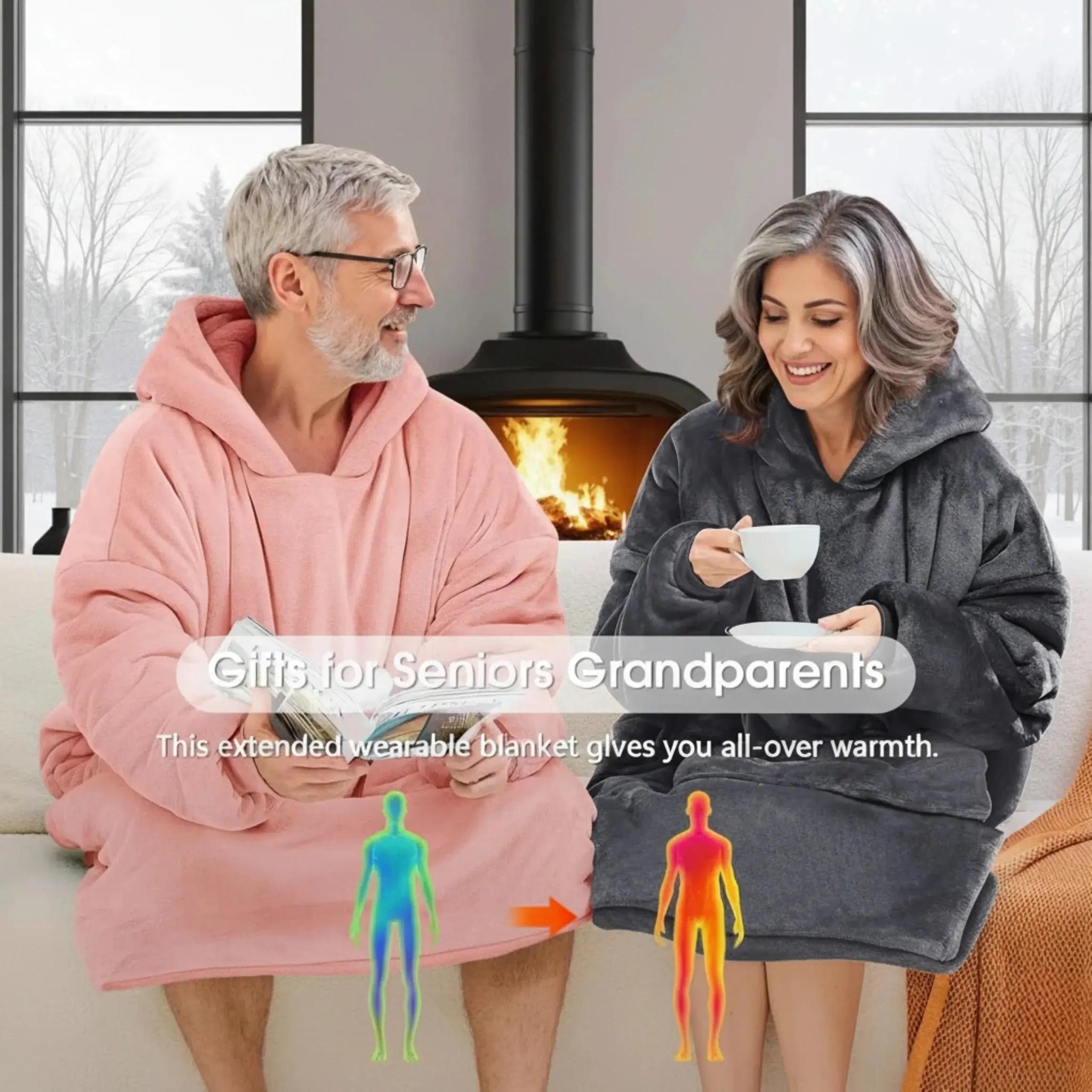 Two seniors wearing oversized fleece hooded jackets, one pink and one charcoal, relaxing by a fireplace.